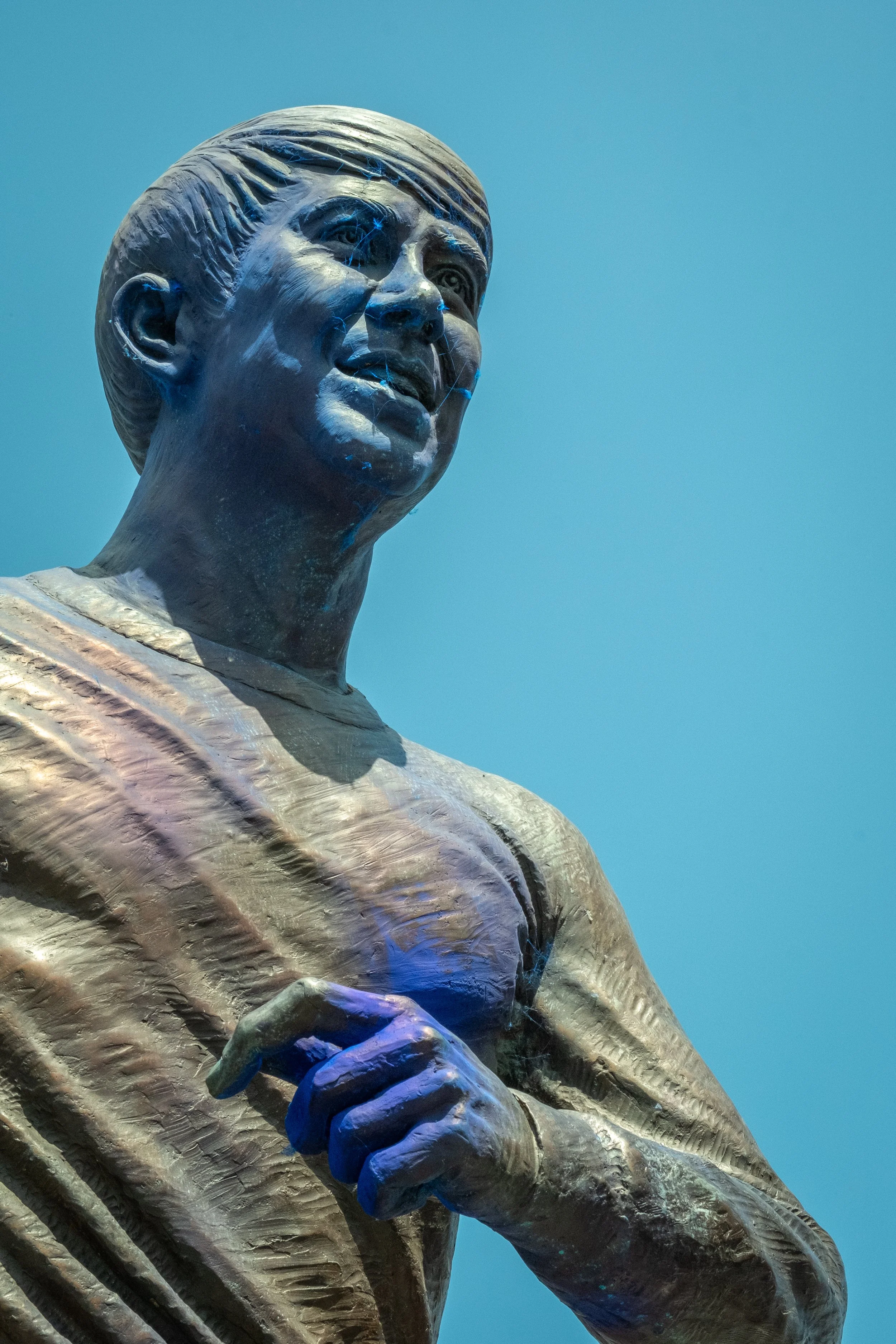 Close-up of a bronze statue of a woman with short hair, wearing traditional clothing, against a blue sky.