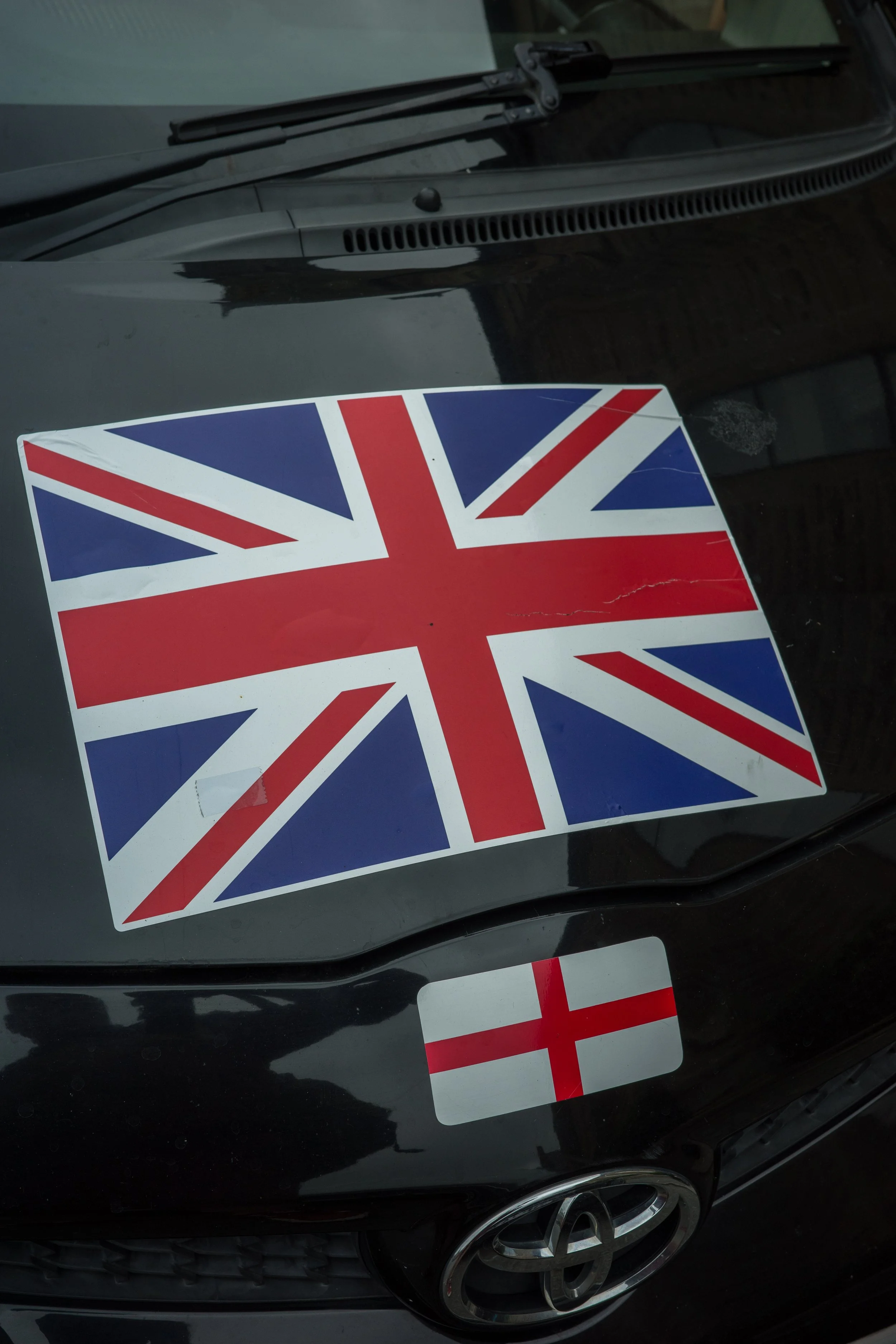Close-up of a black car with stickers of the British flag and a red and white striped pattern on the hood and front fender.