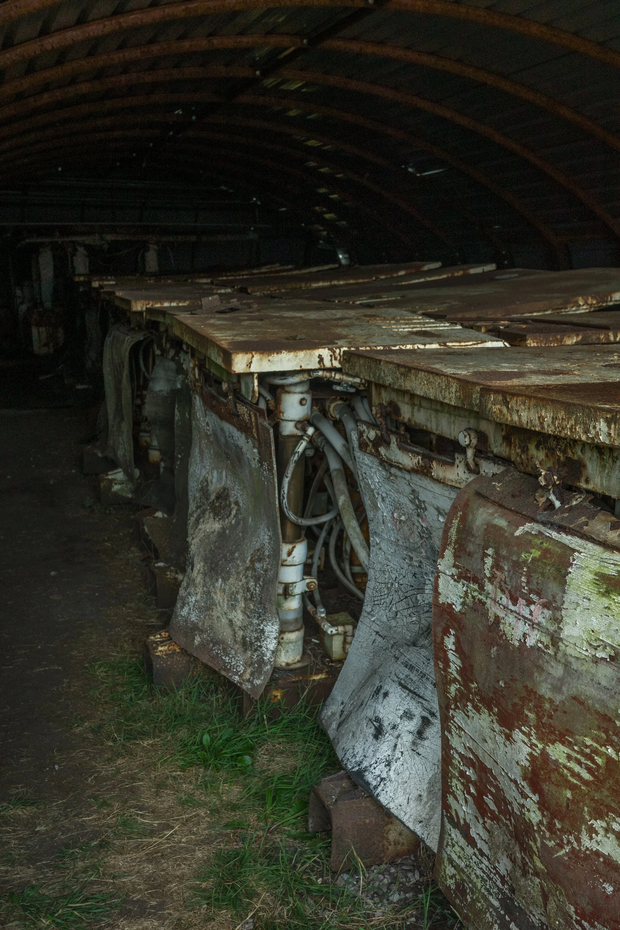A rusted and weathered train car under a dark, arched wooden ceiling, with peeling paint and exposed mechanical parts.