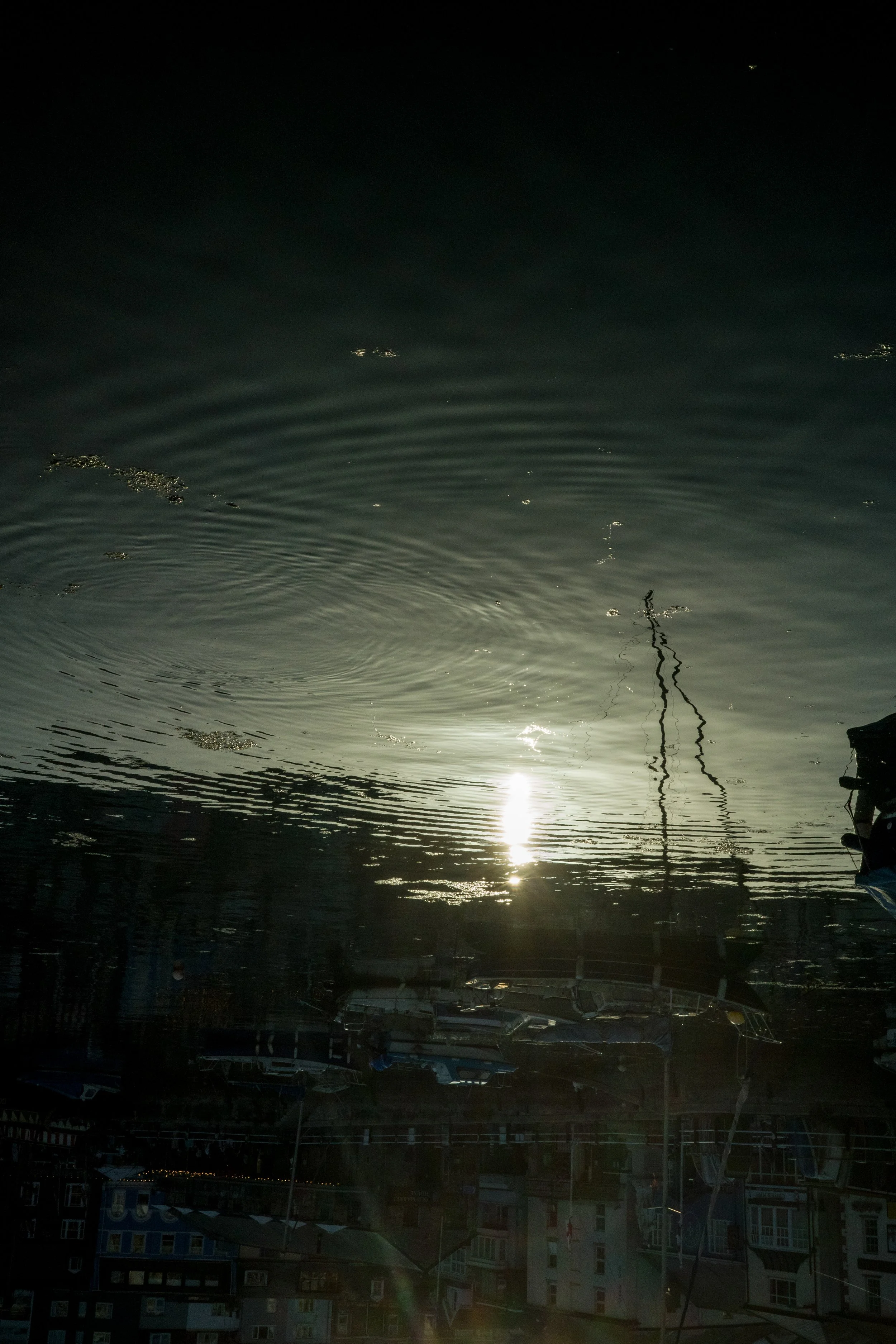 Reflection of boats and buildings in a marina water at sunset.