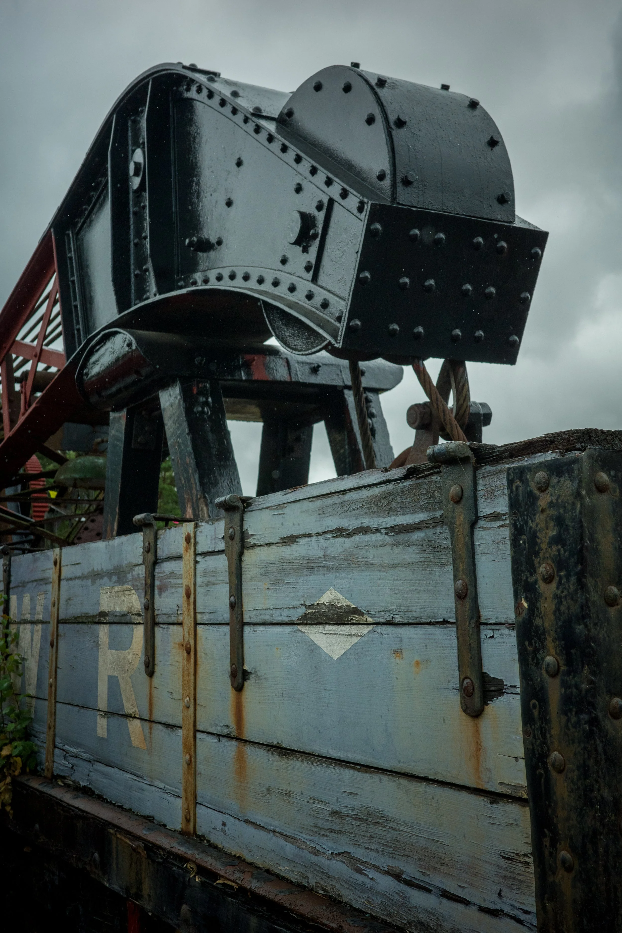 Close-up of an old, weathered wooden train car with rusted metal reinforcements and faded lettering, set against a cloudy sky.