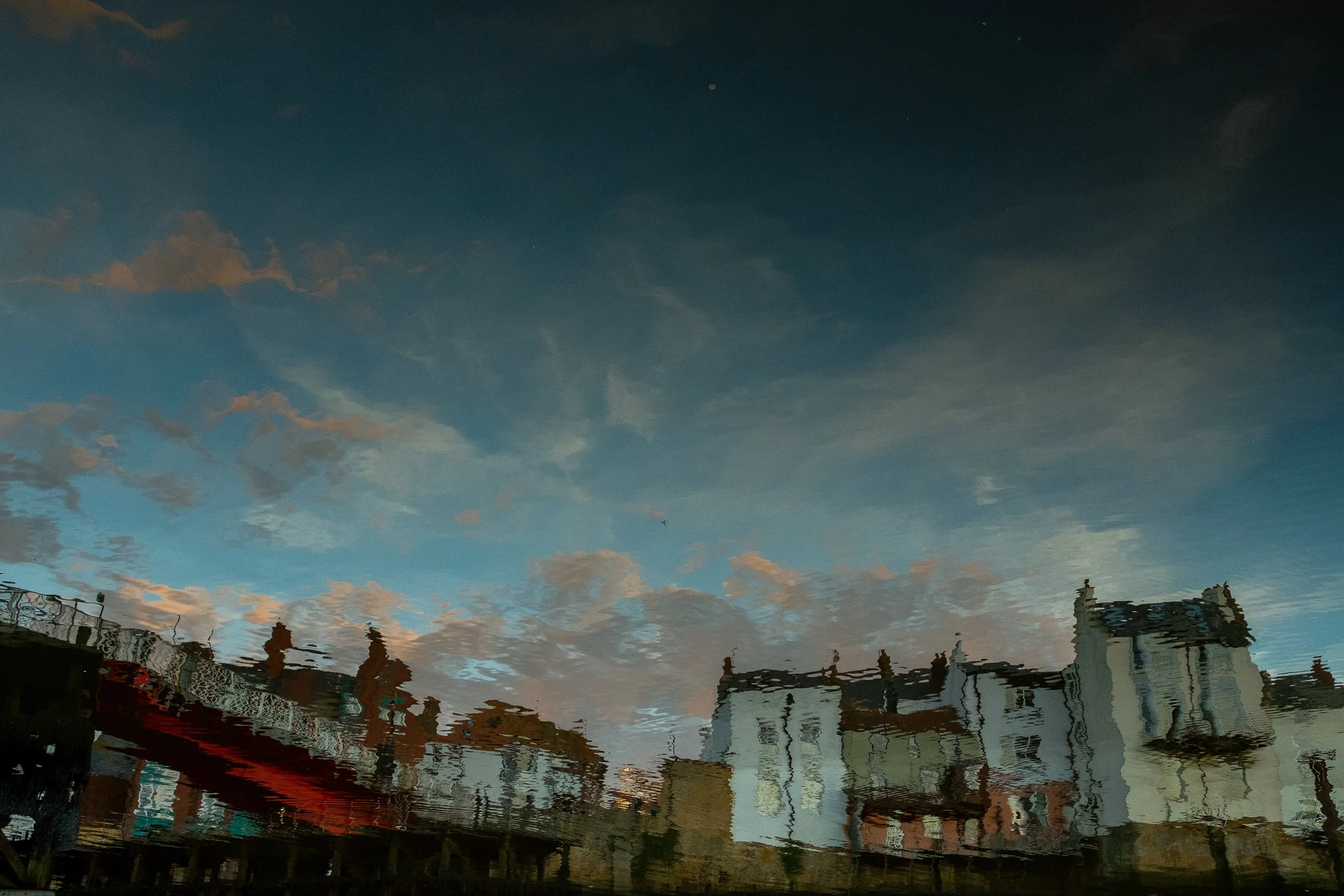 Reflection of a blue sky with clouds and buildings on a water surface.