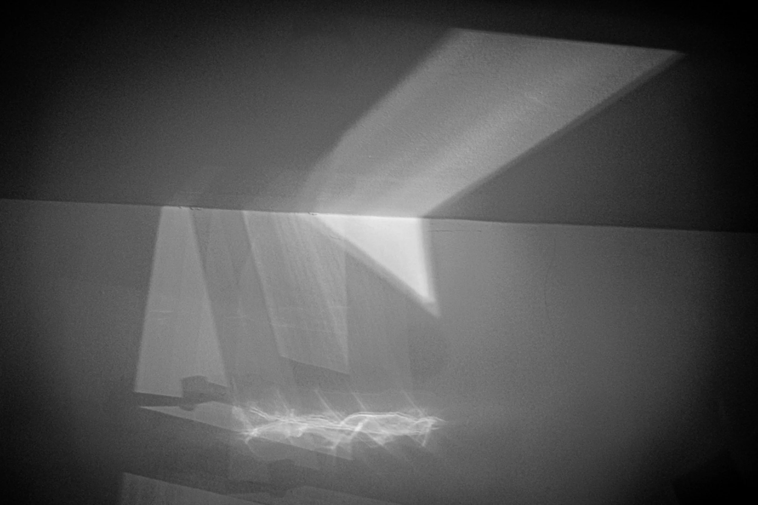 Black and white photo of a ceiling light fixture casting intricate patterns of light and shadow on the ceiling.