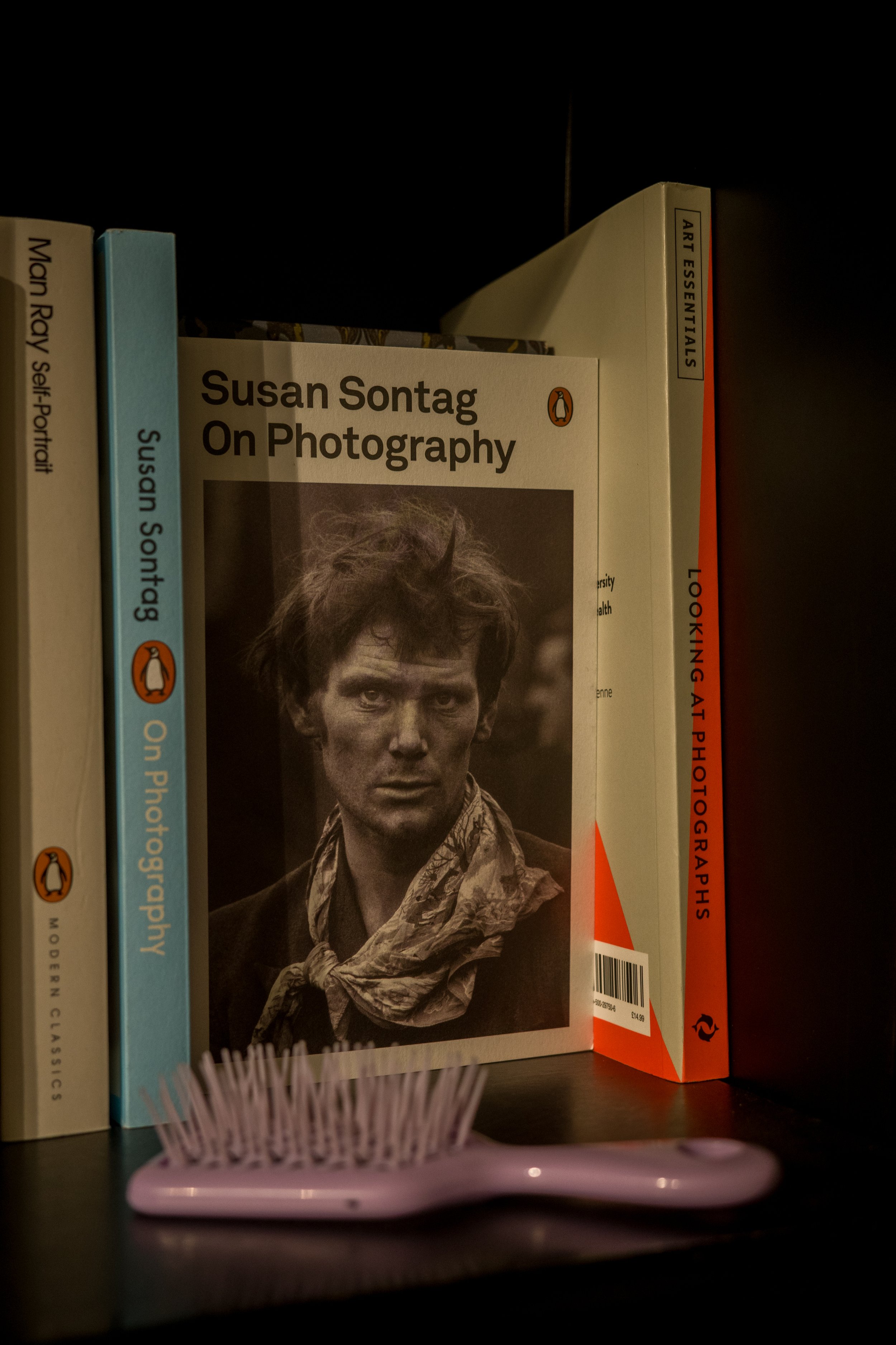 Close-up photograph of a bookshelf containing books about photography, with a partial view of a pink hairbrush in the foreground.