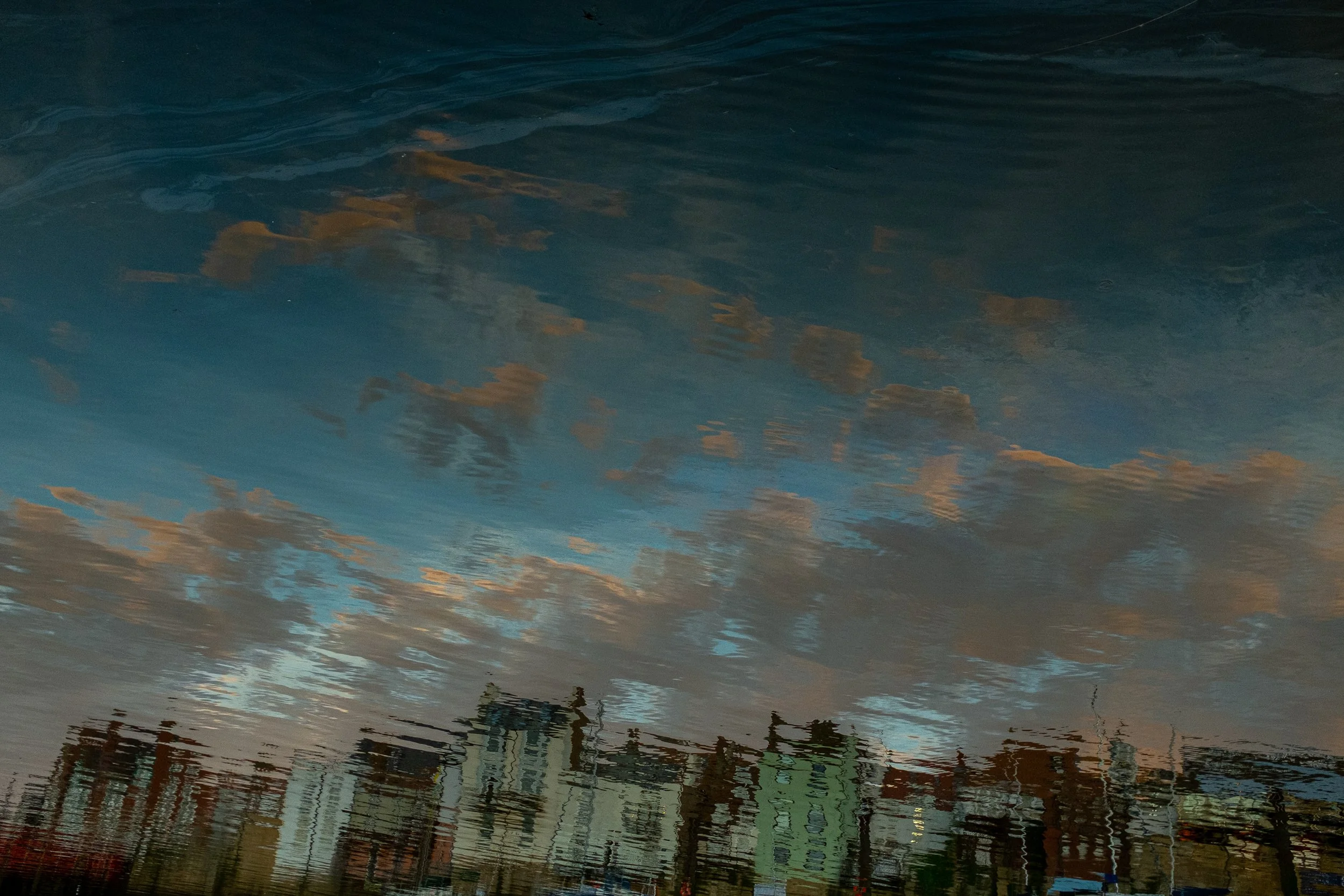 Reflected sky with clouds and buildings on a water surface.