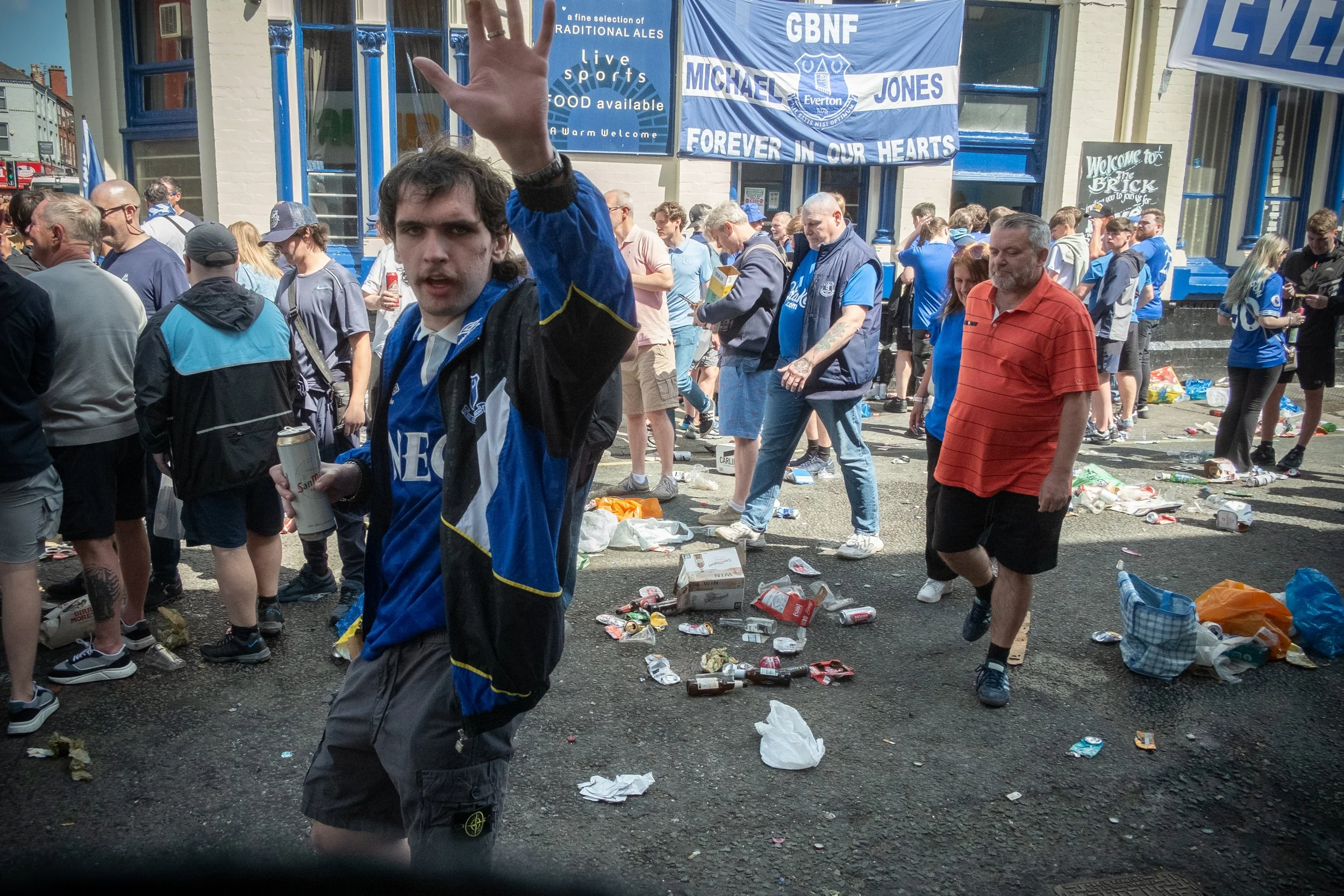 Crowd of sports fans outside a stadium, some drinking and surrounded by litter, with banners and signs in the background, celebrating or mourning a sports event.