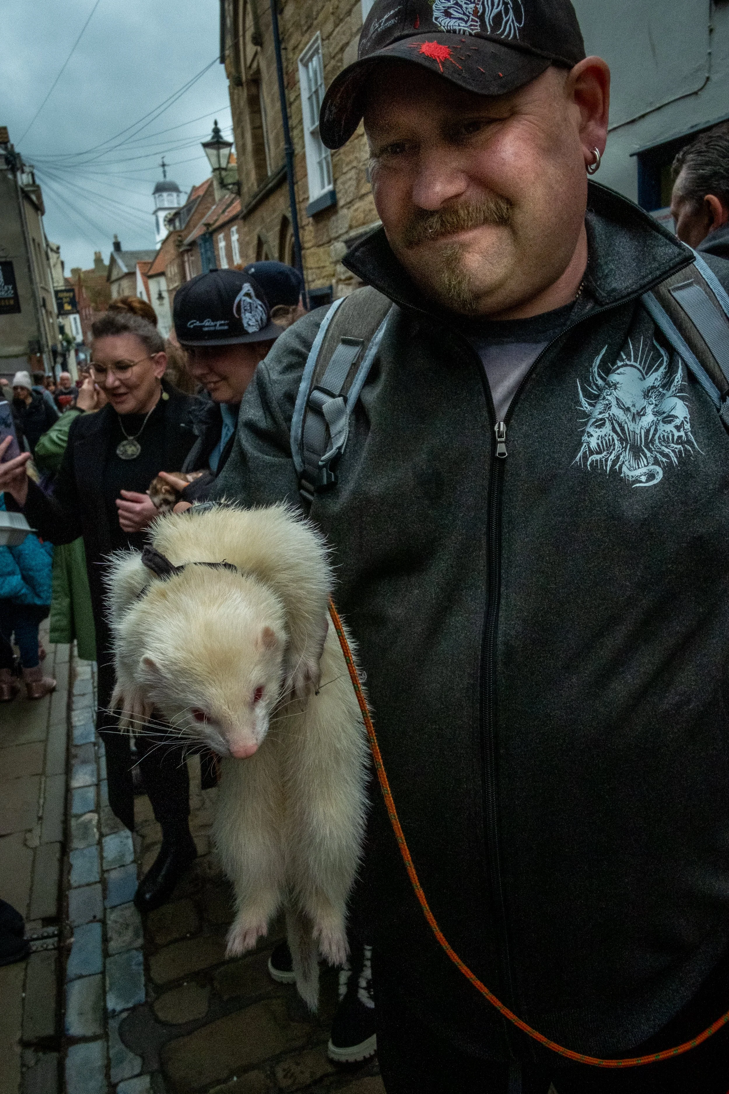 A man holding a ferret in a crowded street with historic buildings and people in the background.