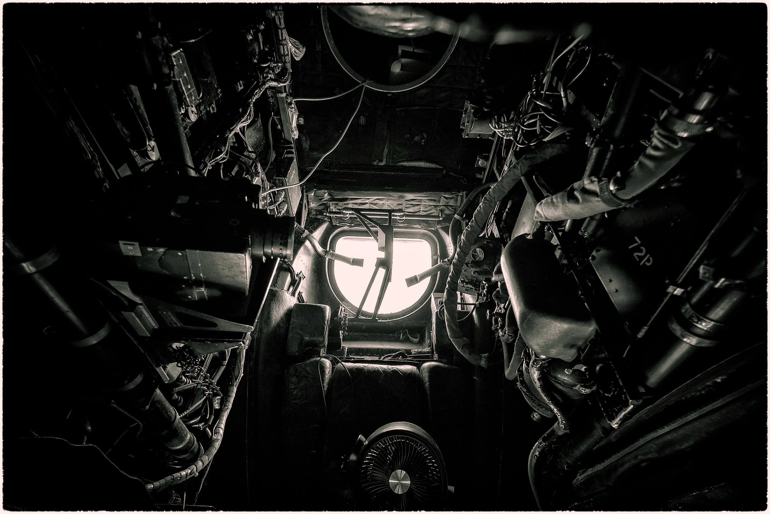 Inside view of an aircraft cockpit showing complex instrumentation, wires, and controls with a window at the back.