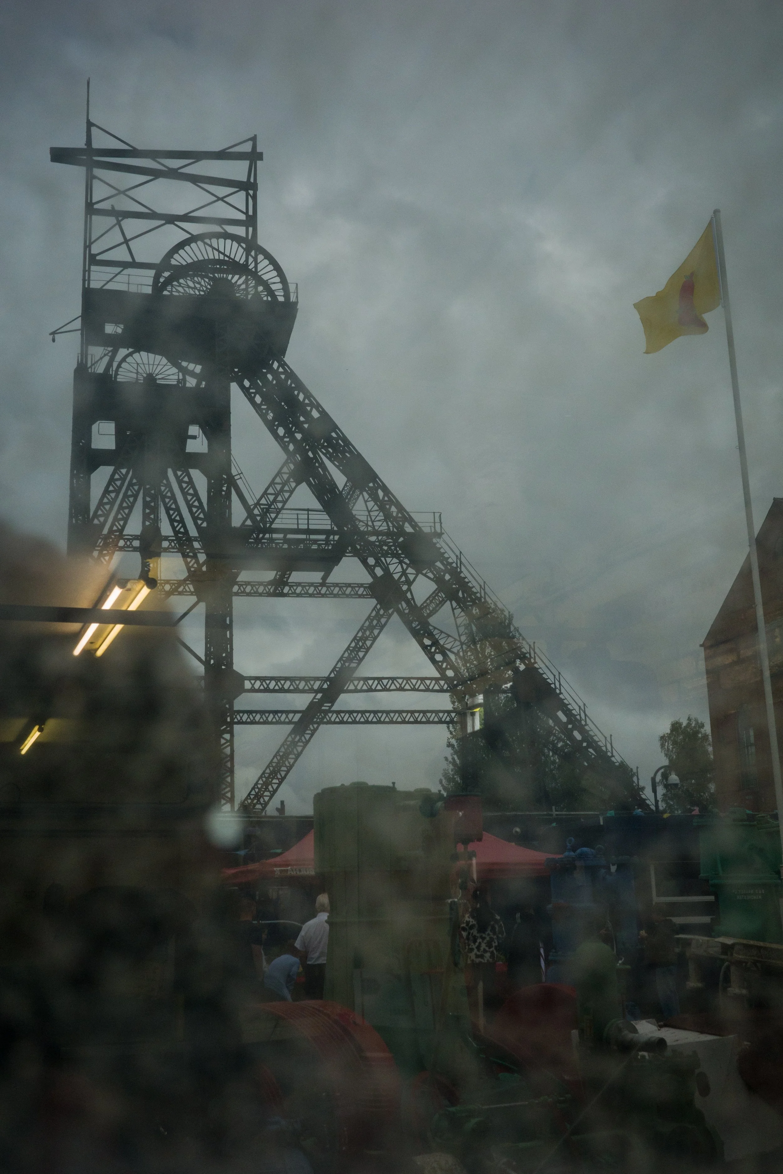 View of an old mining or industrial structure, possibly a headframe from a mine shaft, under a cloudy sky with a yellow flag on the right side.