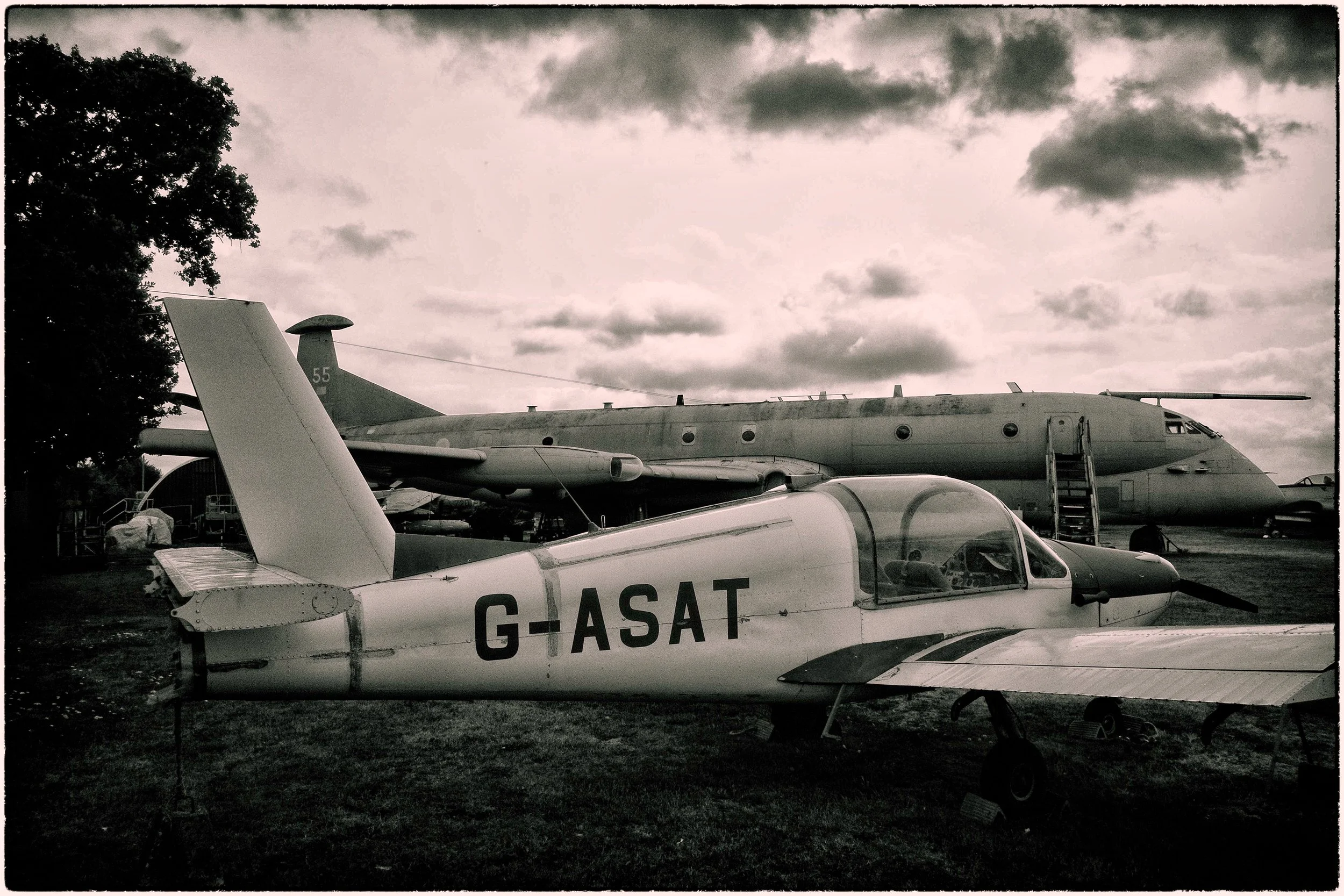 A military jet plane with registration G-ASA T parked outdoors, with another aircraft and cloudy sky in the background.