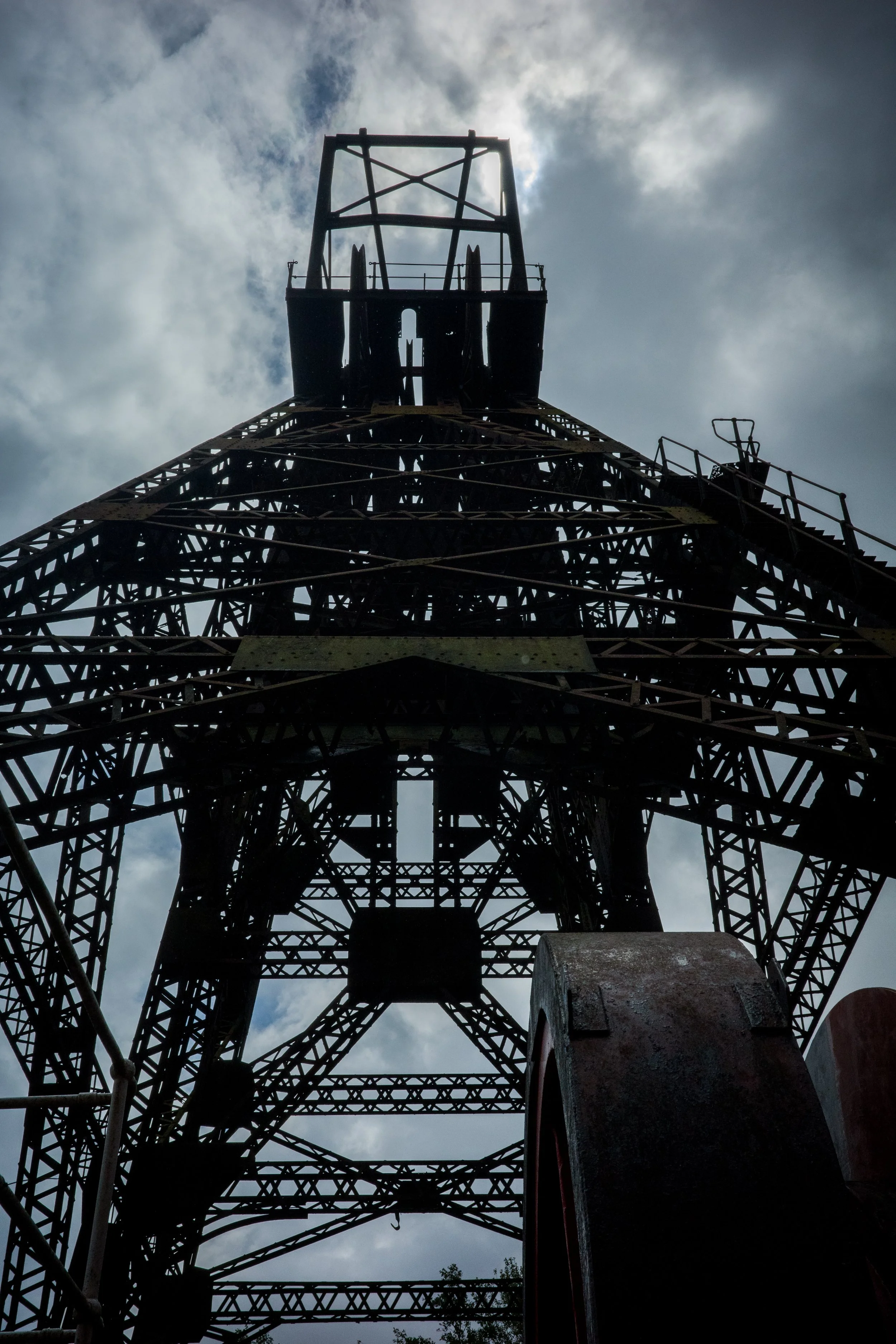 Looking up at an old, tall metal tower structure against a cloudy sky.