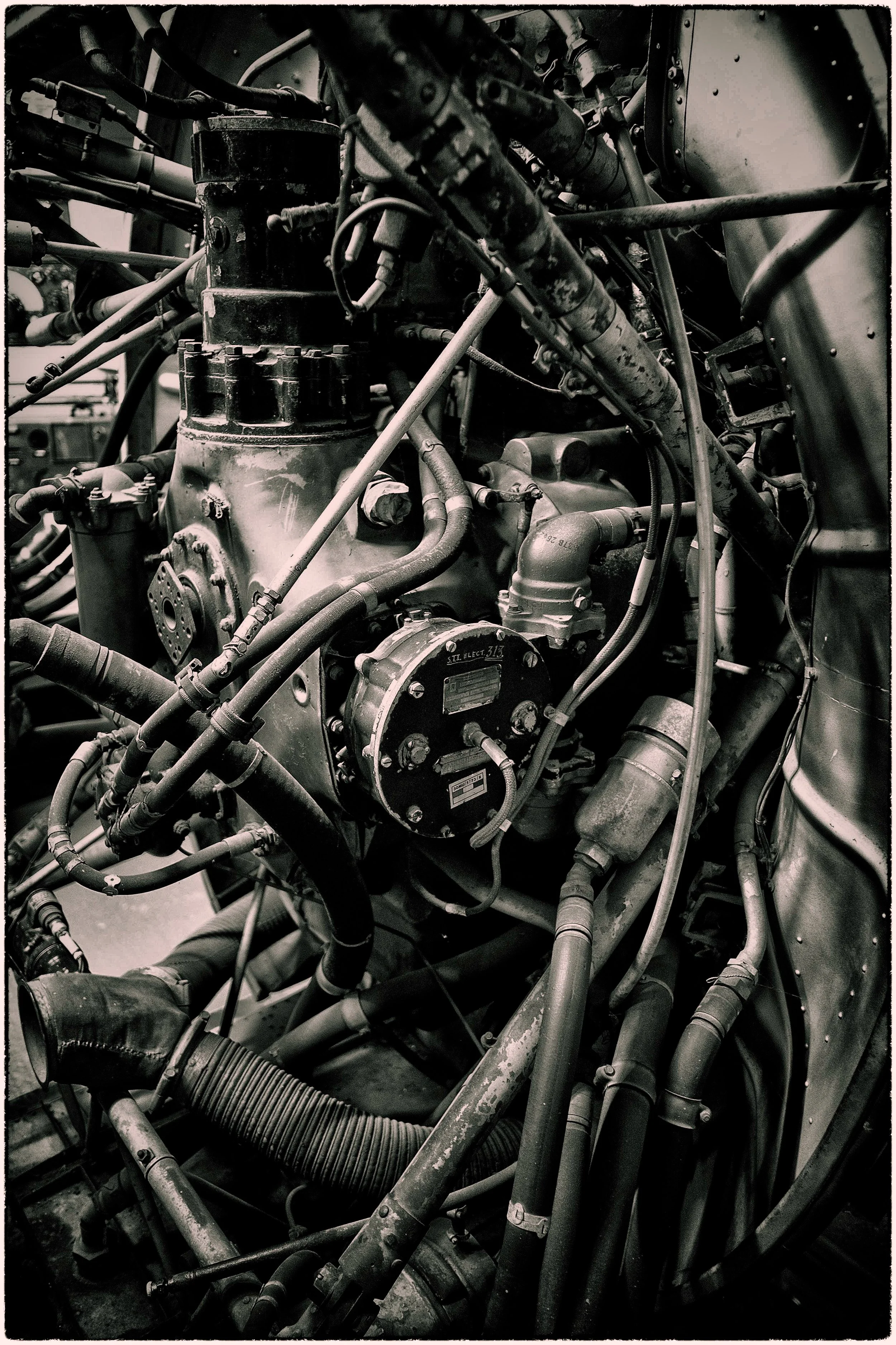 Close-up of an aircraft jet engine with various pipes, tubes, and mechanical components in black and white.