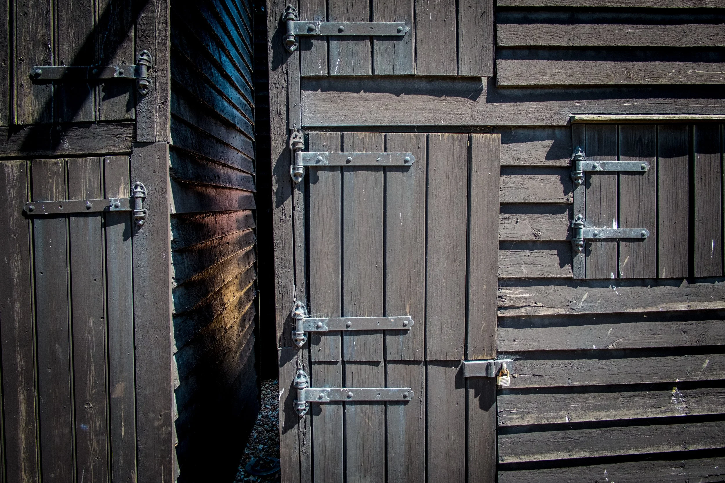 Close-up of a wooden garden shed or outhouse with closed door, metal hinges, latch, and padlock, made of brown painted horizontal wooden planks.