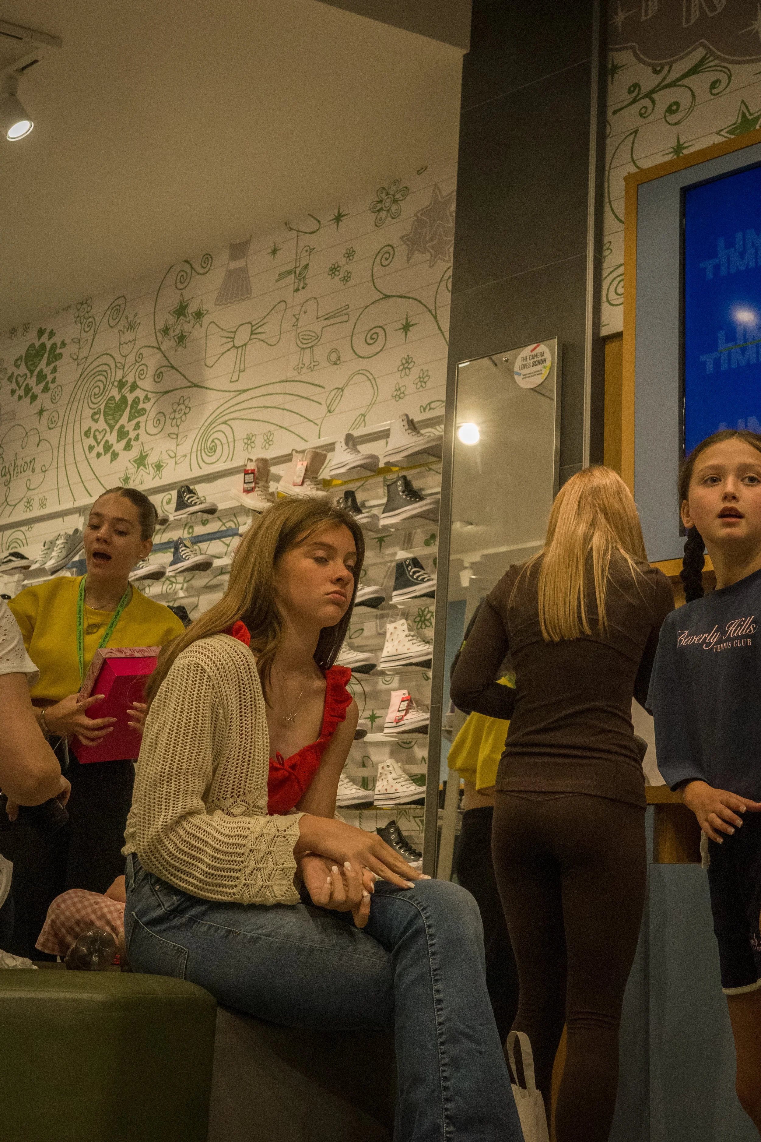 People waiting in line inside a shoe store, with shelves of sneakers on the wall behind them.