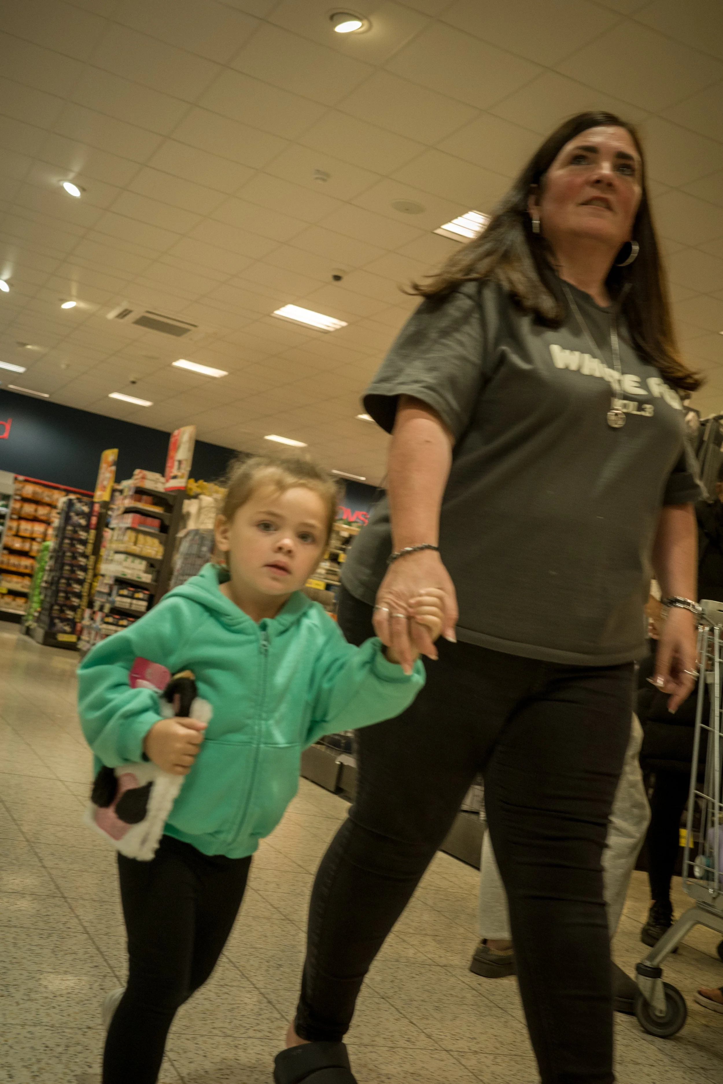 A woman holding hands with a young girl inside a grocery store aisle.