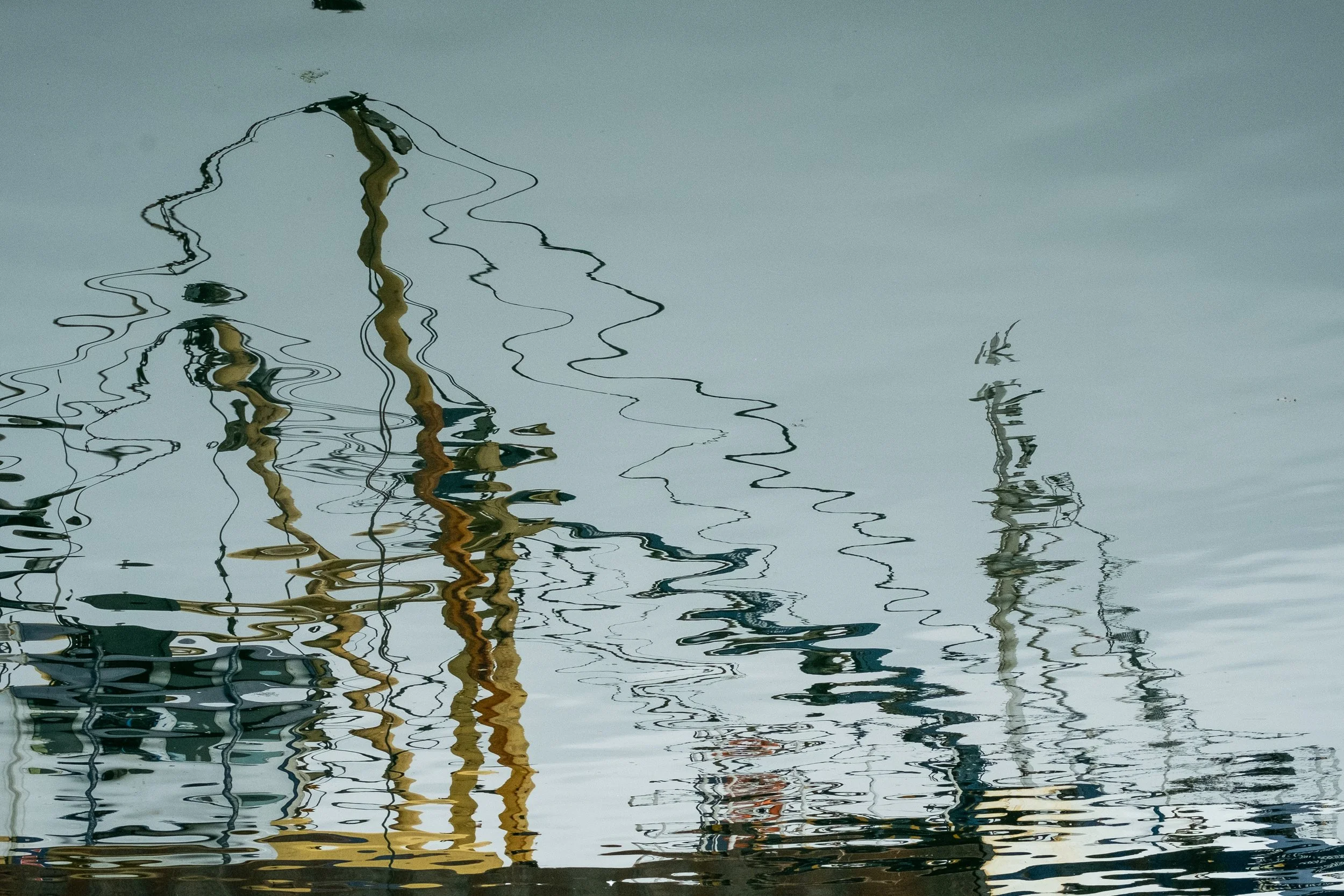 Reflections of sailboat masts and rigging in calm water