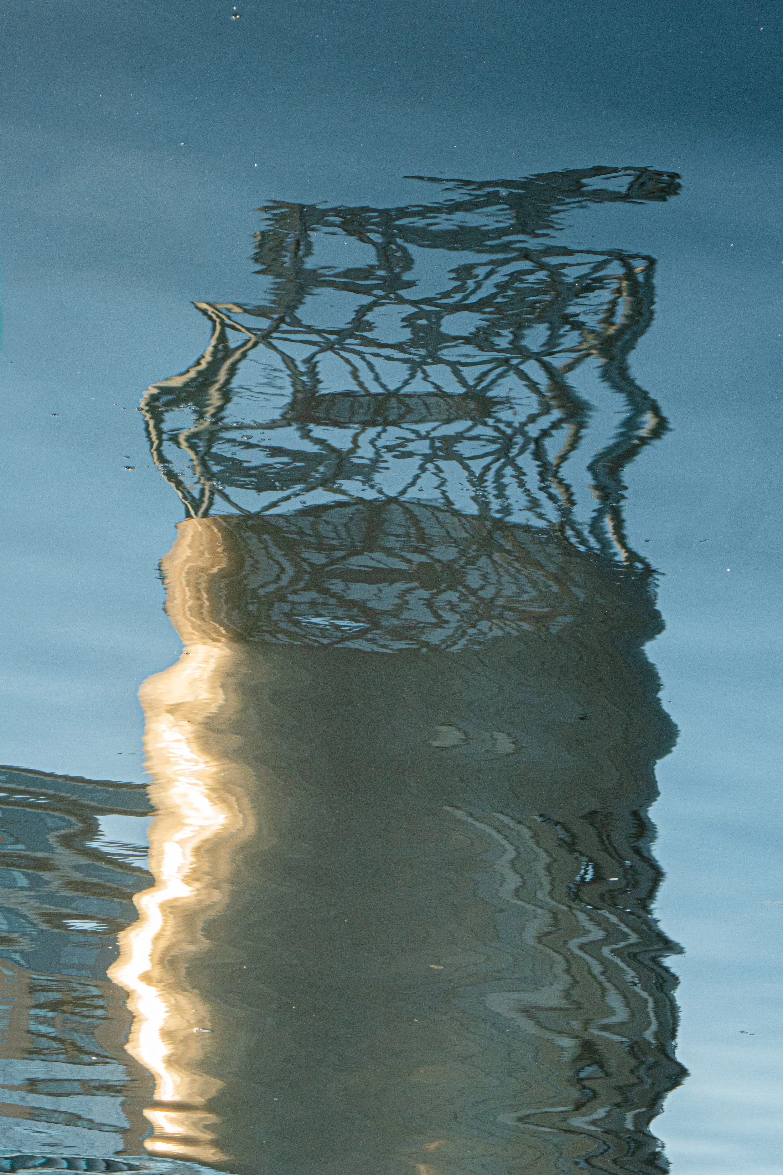 Reflection of a telecommunications tower in water with ripples.