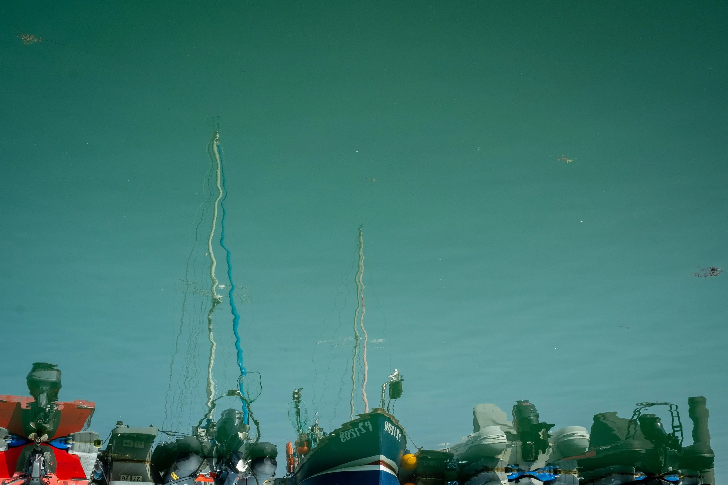 Reflected image of boats docked at a marina, with their masts and hulls visible in the water.