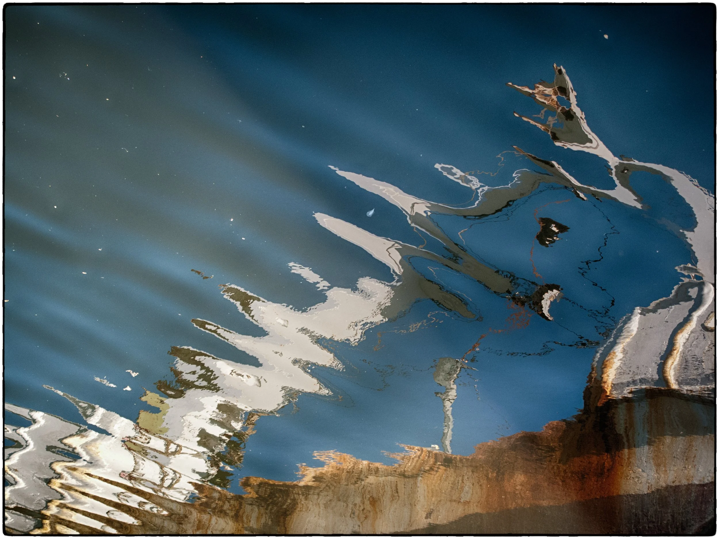 Reflection of boats and sky on water with ripples and waves.