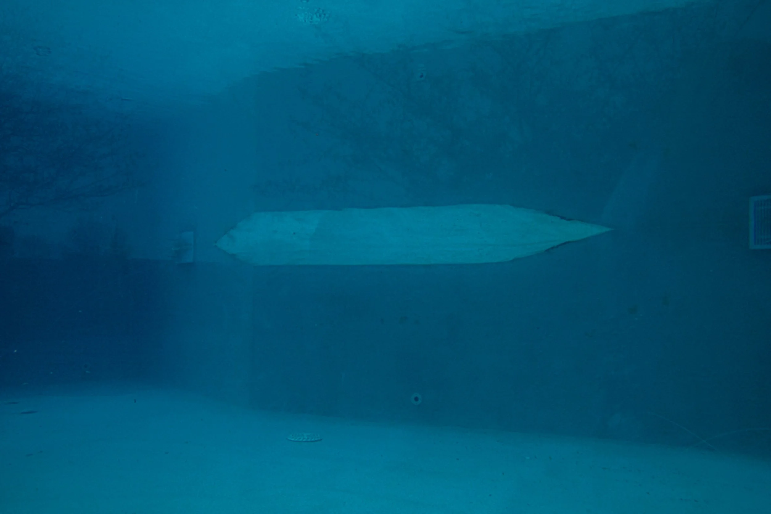 A blue underwater scene with what appears to be a sunken ship or structure in the background, illuminated by blue light.