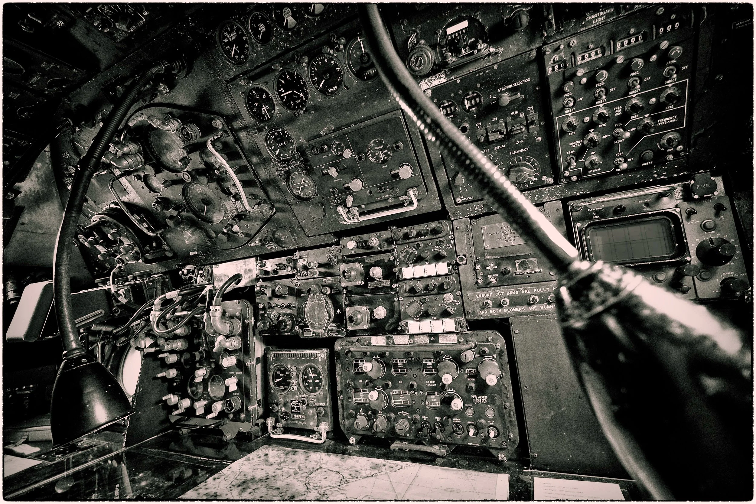 Inside the cockpit of an aircraft showcasing numerous panels filled with gauges, switches, and controls, with a black and white color scheme.