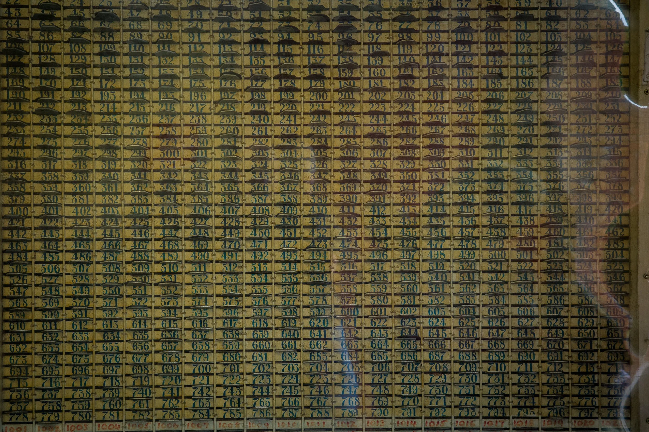 A wall of numbered mailboxes in a grid pattern with handwritten letters, some mailboxes have visible mail inside, and a white graffiti swirl on the right side.
