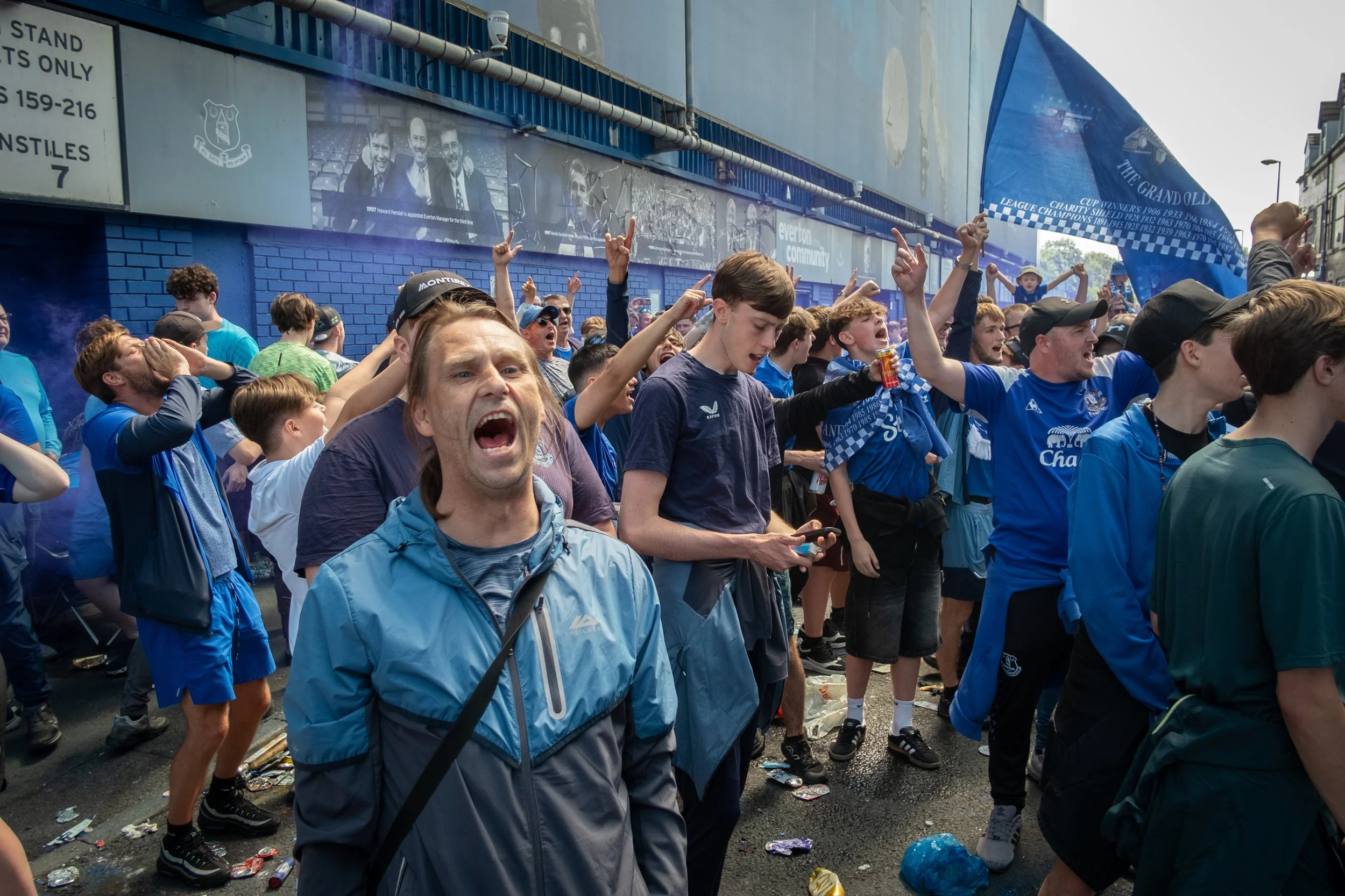 Crowd of excited sports fans, mostly young men, celebrating outside a stadium with team apparel and flags.