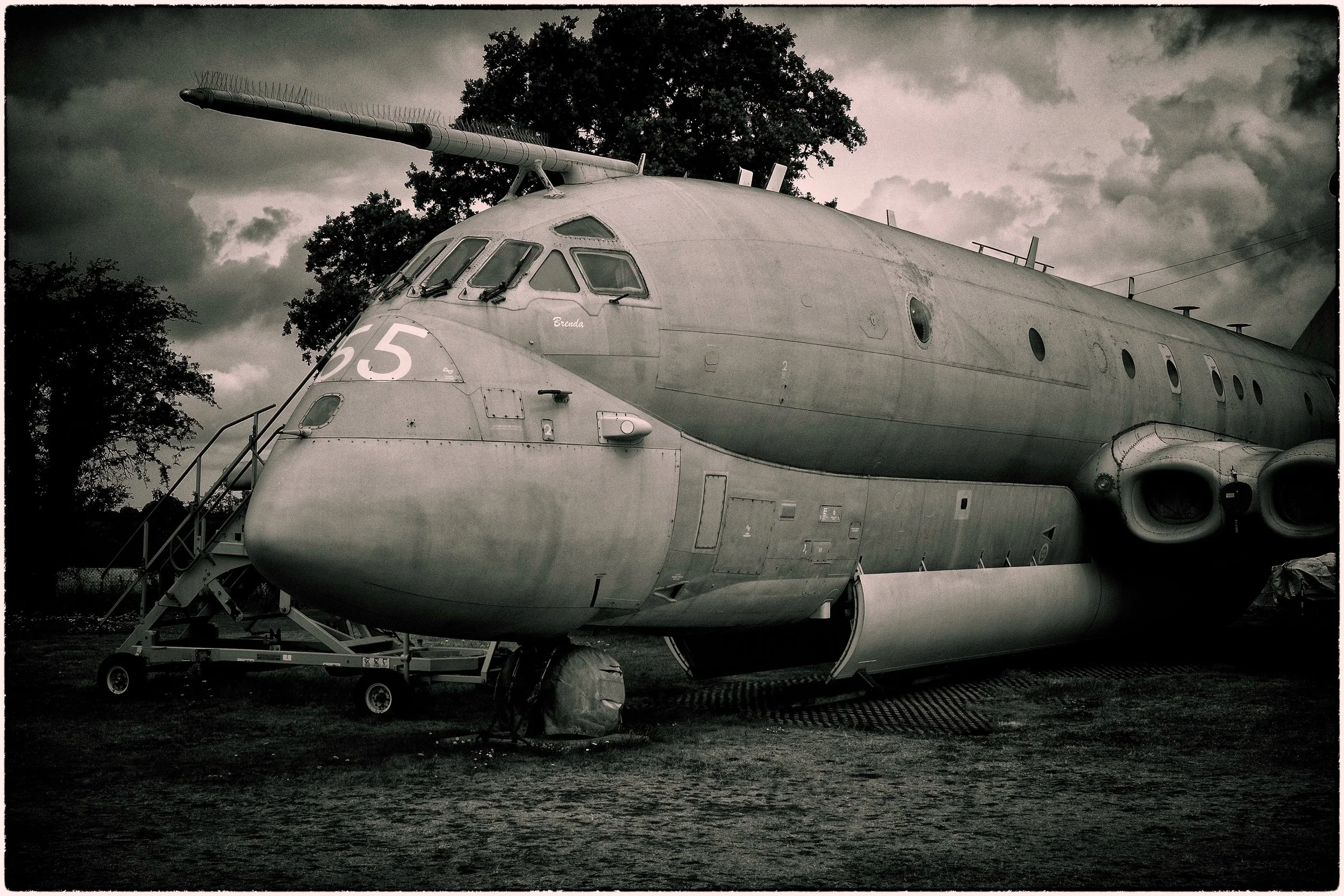 A military cargo helicopter parked outdoors under dark, cloudy skies, with trees in the background.