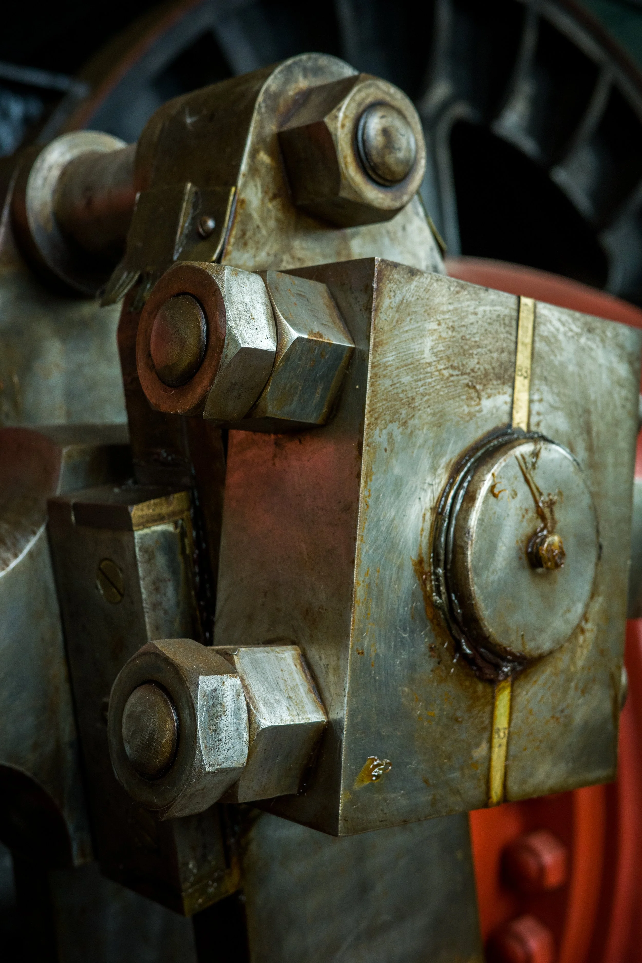 Close-up of a mechanical or industrial machine part with bolts, nuts, and a circular component, showing signs of rust and wear.