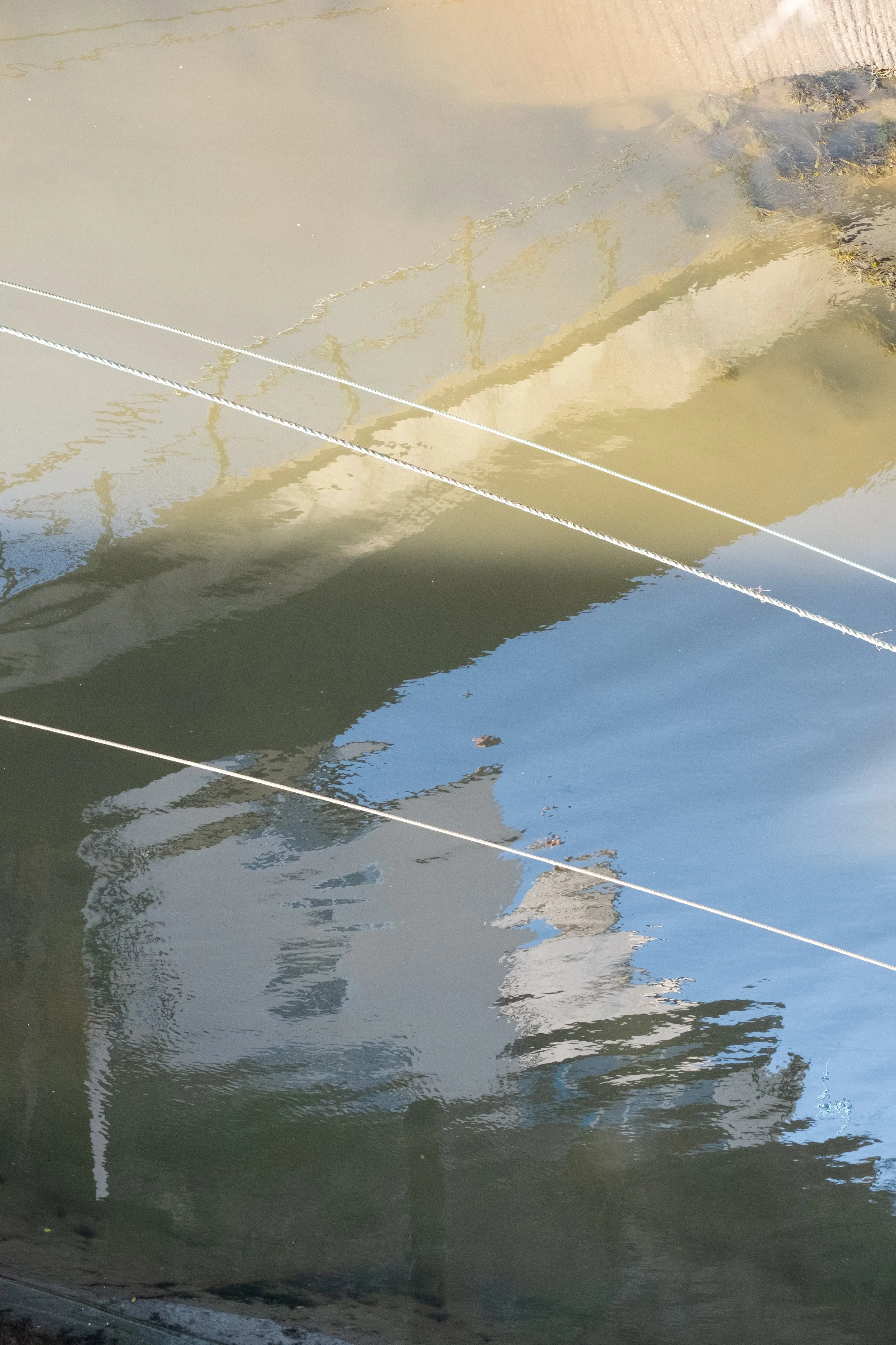 Reflections of a boat and ropes on the water's surface.