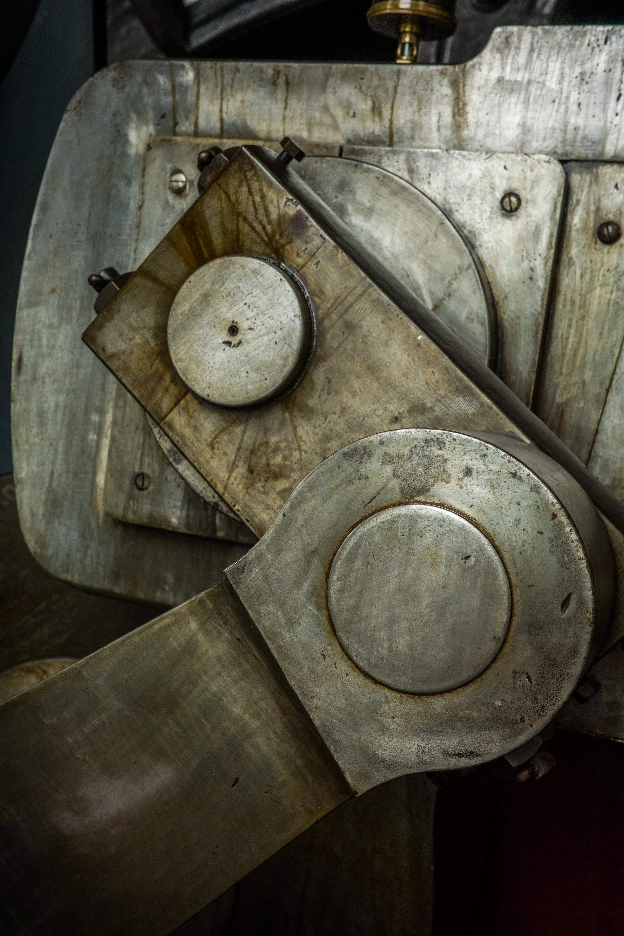 Close-up of a vintage mechanical sewing machine's metal parts, including a large round wheel and a metallic arm, with a worn, stained surface.