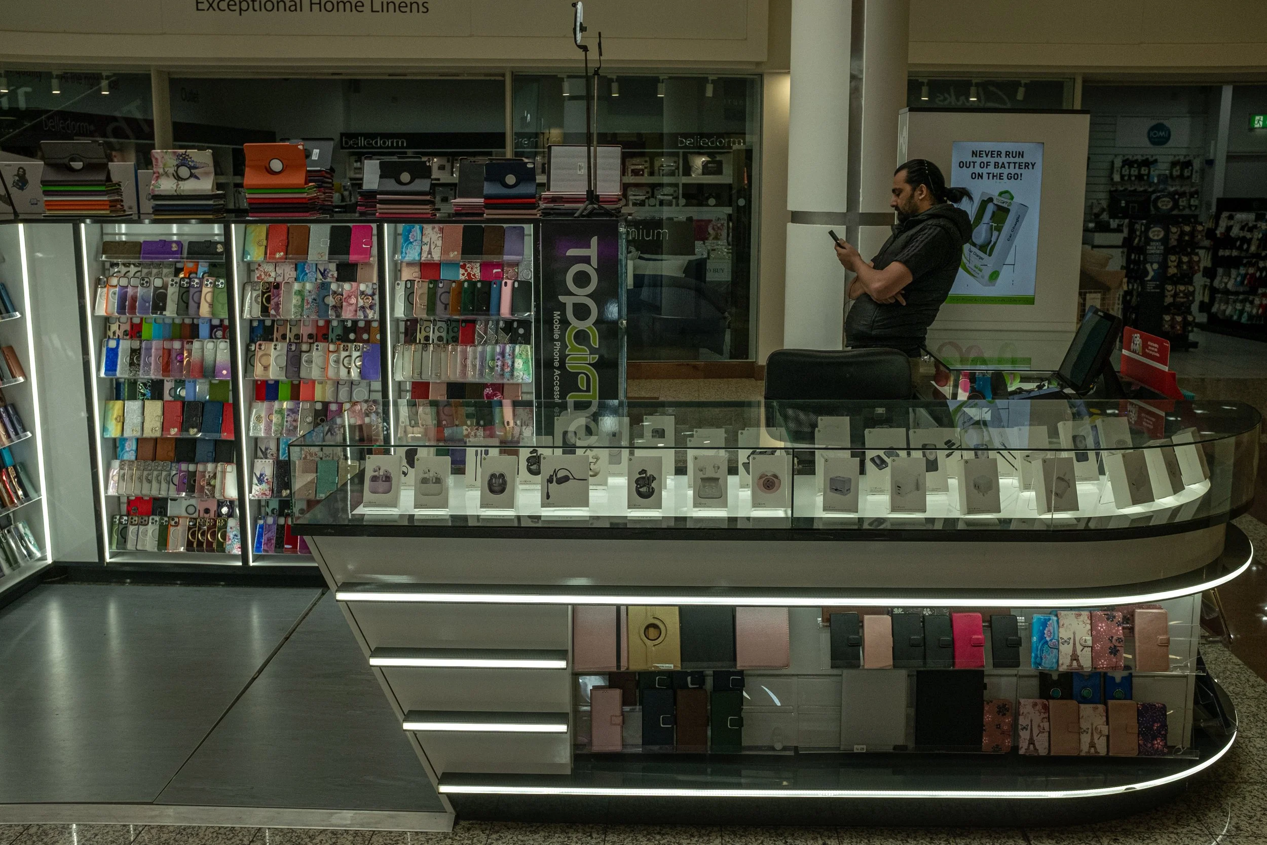 A display of various phone cases and accessories in a store, with a man standing nearby and looking at his phone.