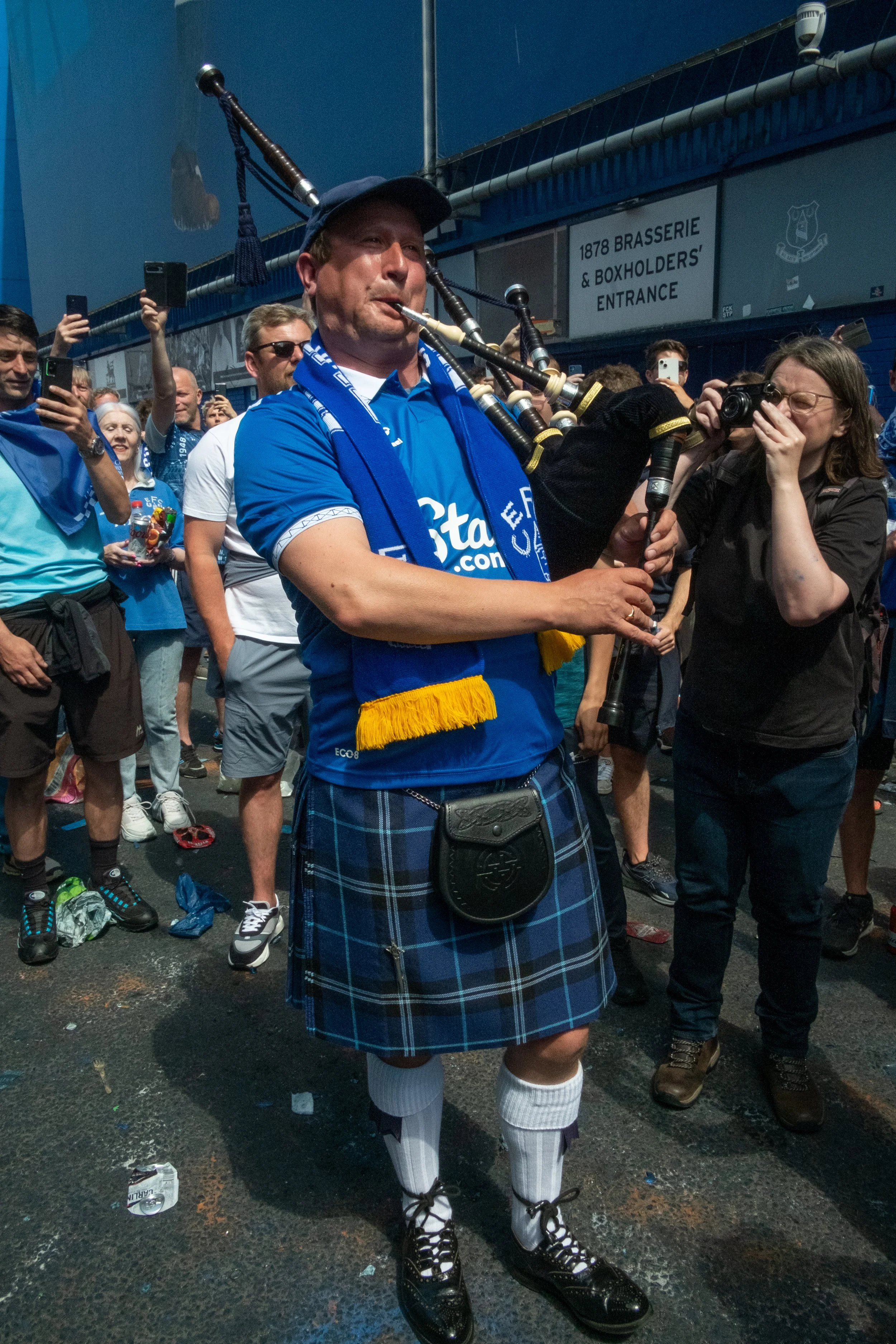 A man wearing a traditional Scottish kilt and playing bagpipes at a crowded outdoor event.
