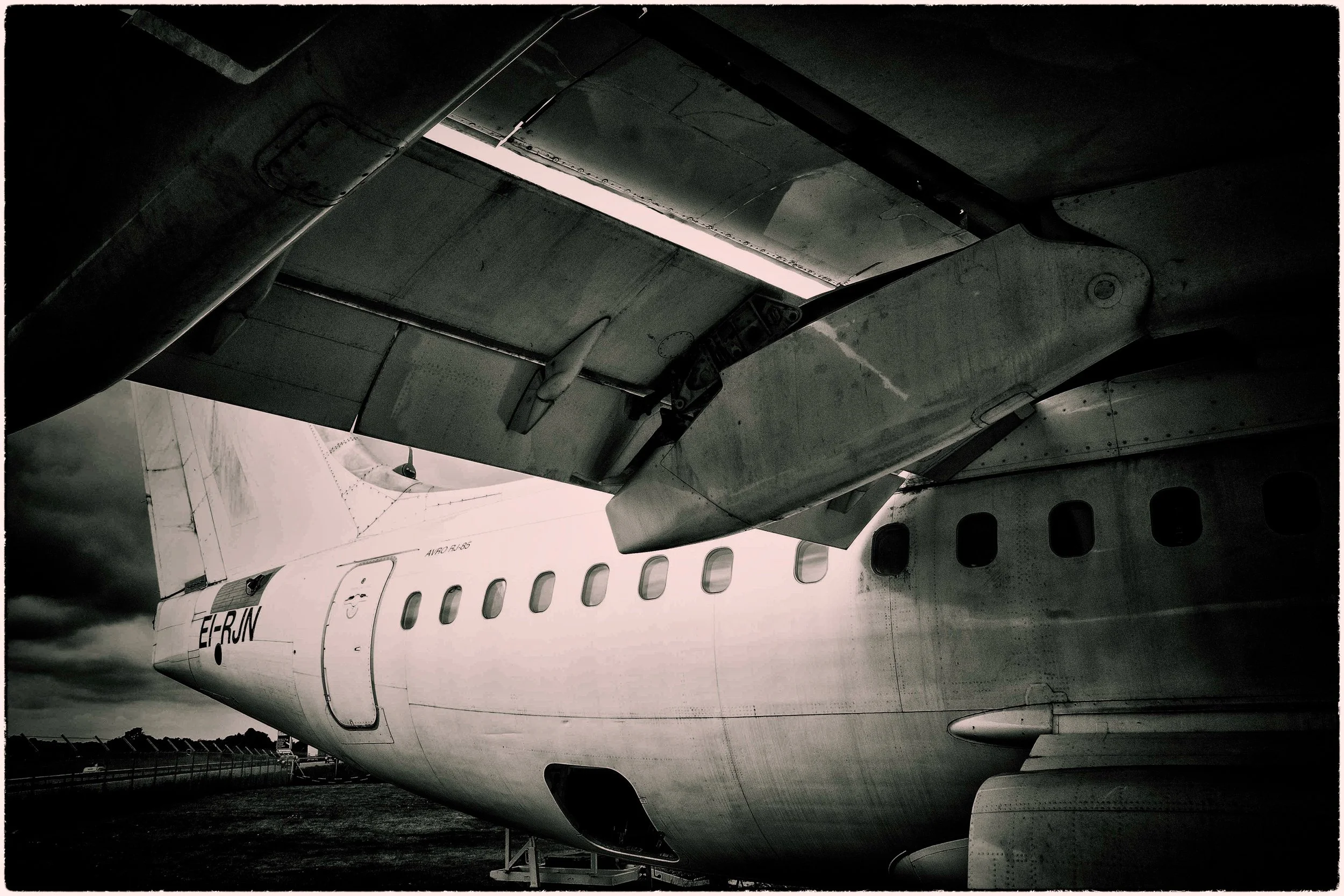 A black and white photo of multiple airplanes parked on the tarmac, focusing on the underside of an aircraft's wing and fuselage.