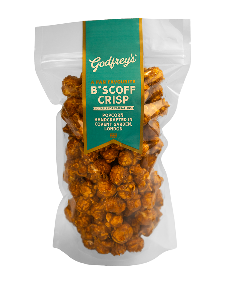 A clear plastic bag of caramel-coated popcorn, with a teal and yellow label from Godfrey's that reads "A fan favorite B*SCOFF CRISP suitable for vegetarians, handcrafted in Covent Garden, London."