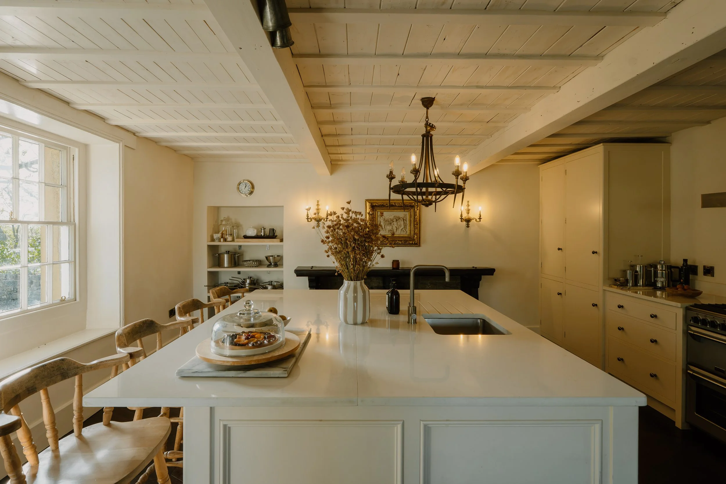 Elegant farmhouse kitchen with a large white island, sink, chandelier, cream cabinetry, dining chairs, and fireplace
