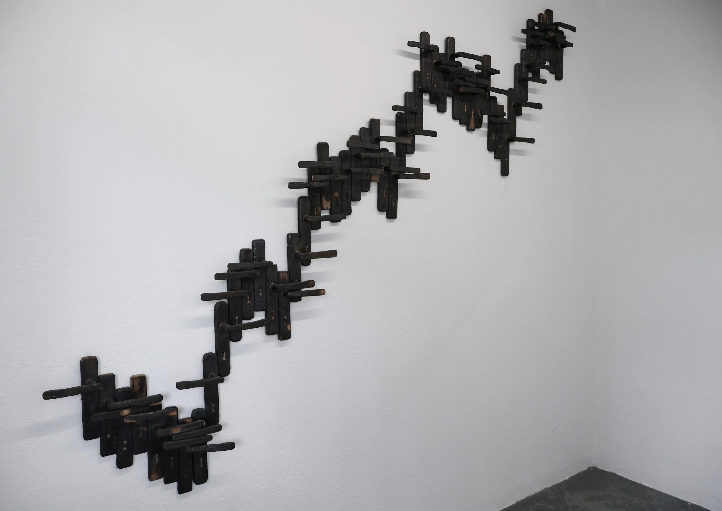 A Statistic of Trauma, 2023. 50 burnt door handles, 215 × 260 cm.