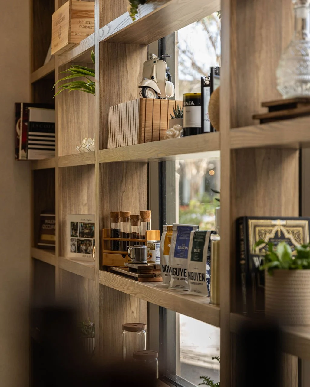 Wooden shelves holding coffee supplies, plants, and decorative items next to a window.