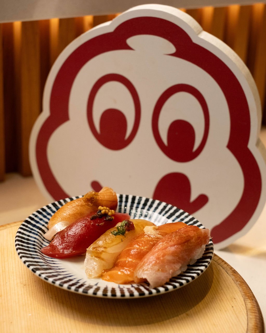 A plate of assorted sushi with a cartoon mascot in the background.