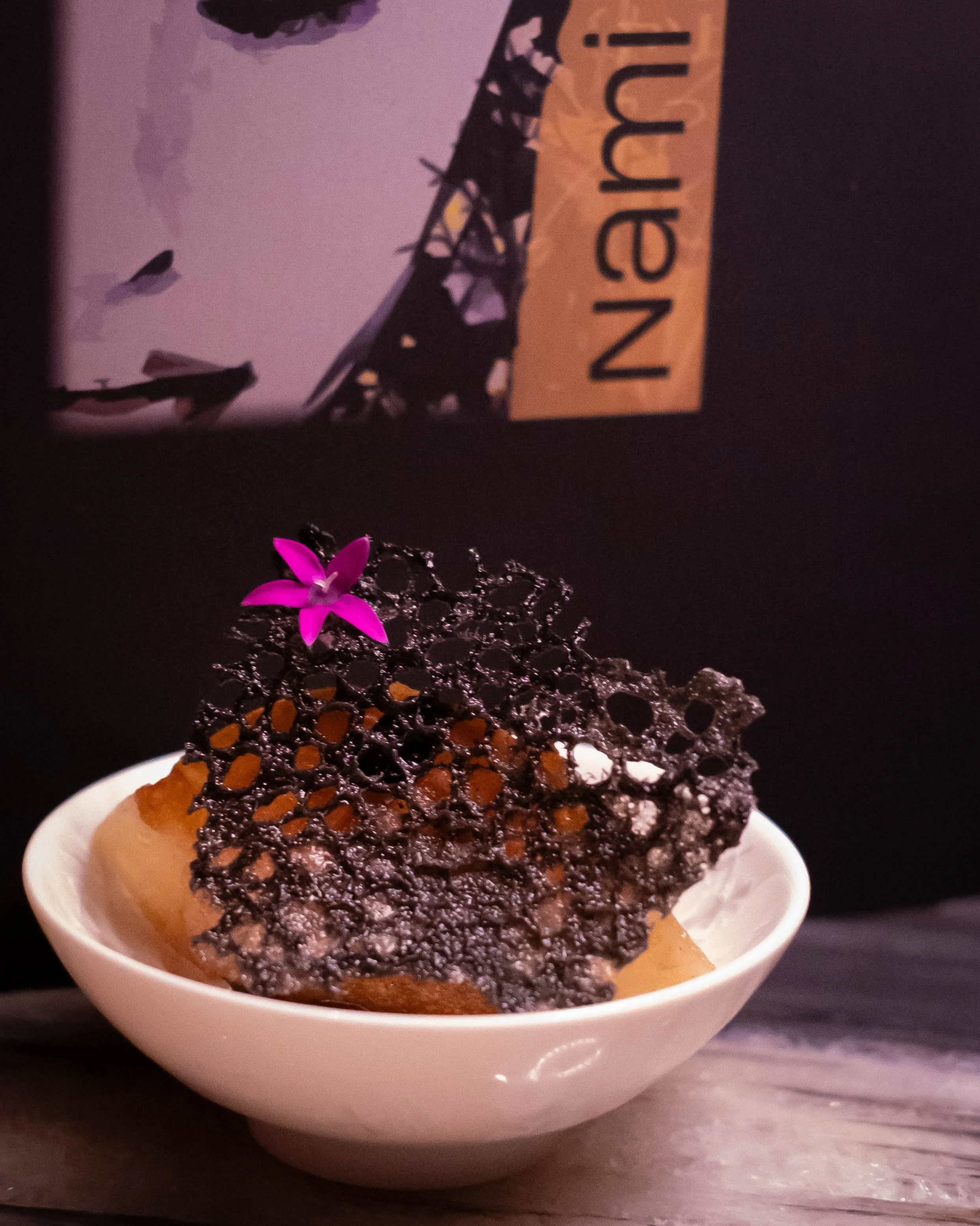 Dessert in a white bowl topped with a black lattice sugar decoration and a pink flower