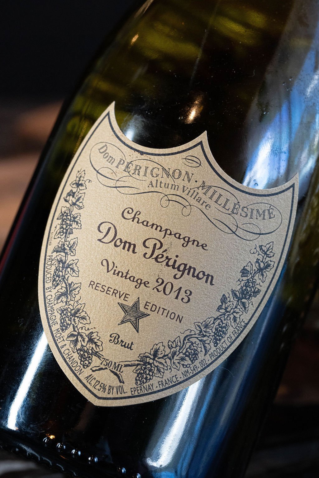 A bottle of Dom Pérignon vintage 2013 champagne with a cream-colored label featuring floral and grapevine illustrations, and text indicating it is a reserved edition brut from France.