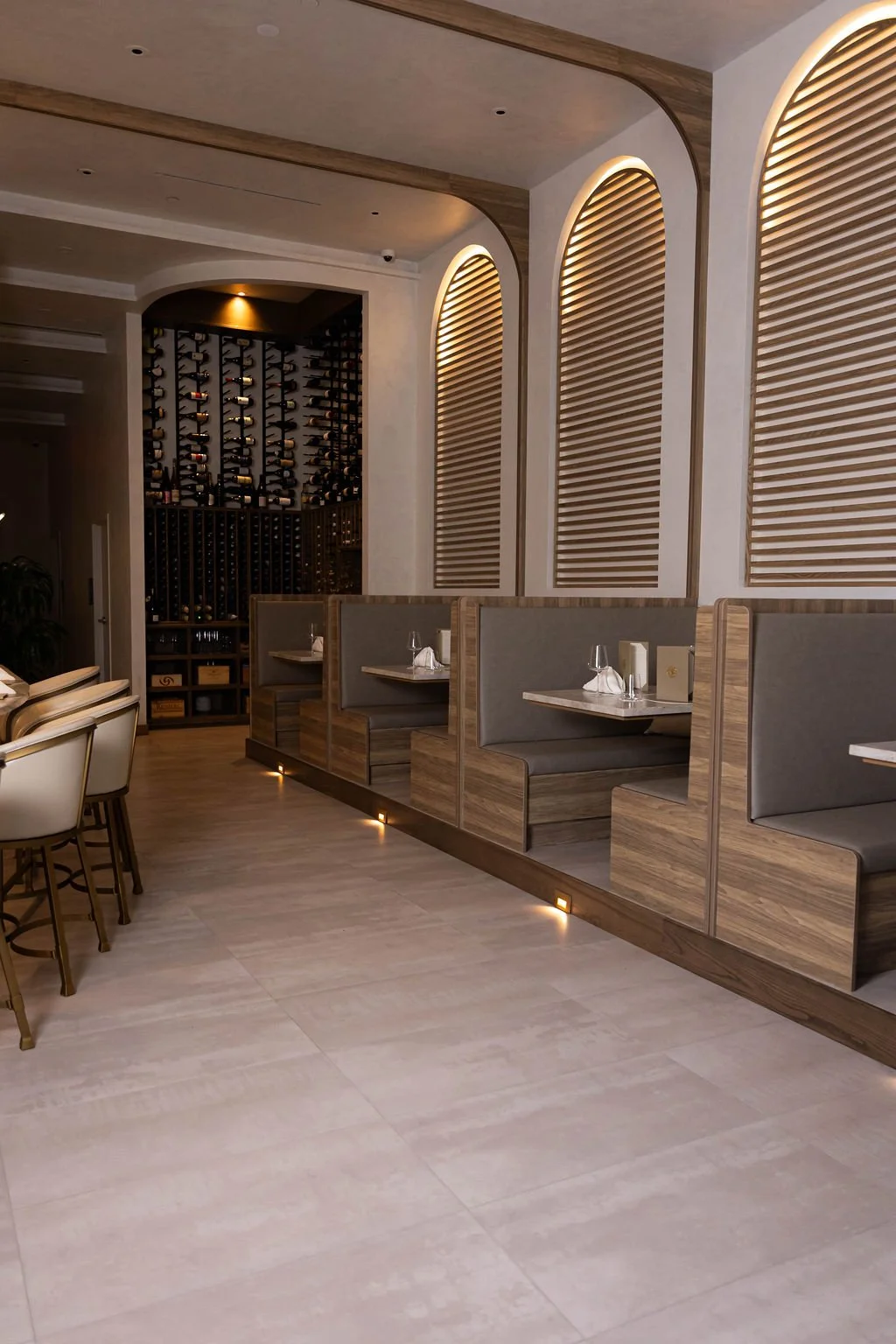 Upscale restaurant seating area with wooden booths, table settings, wine rack on the wall, and ambient lighting.