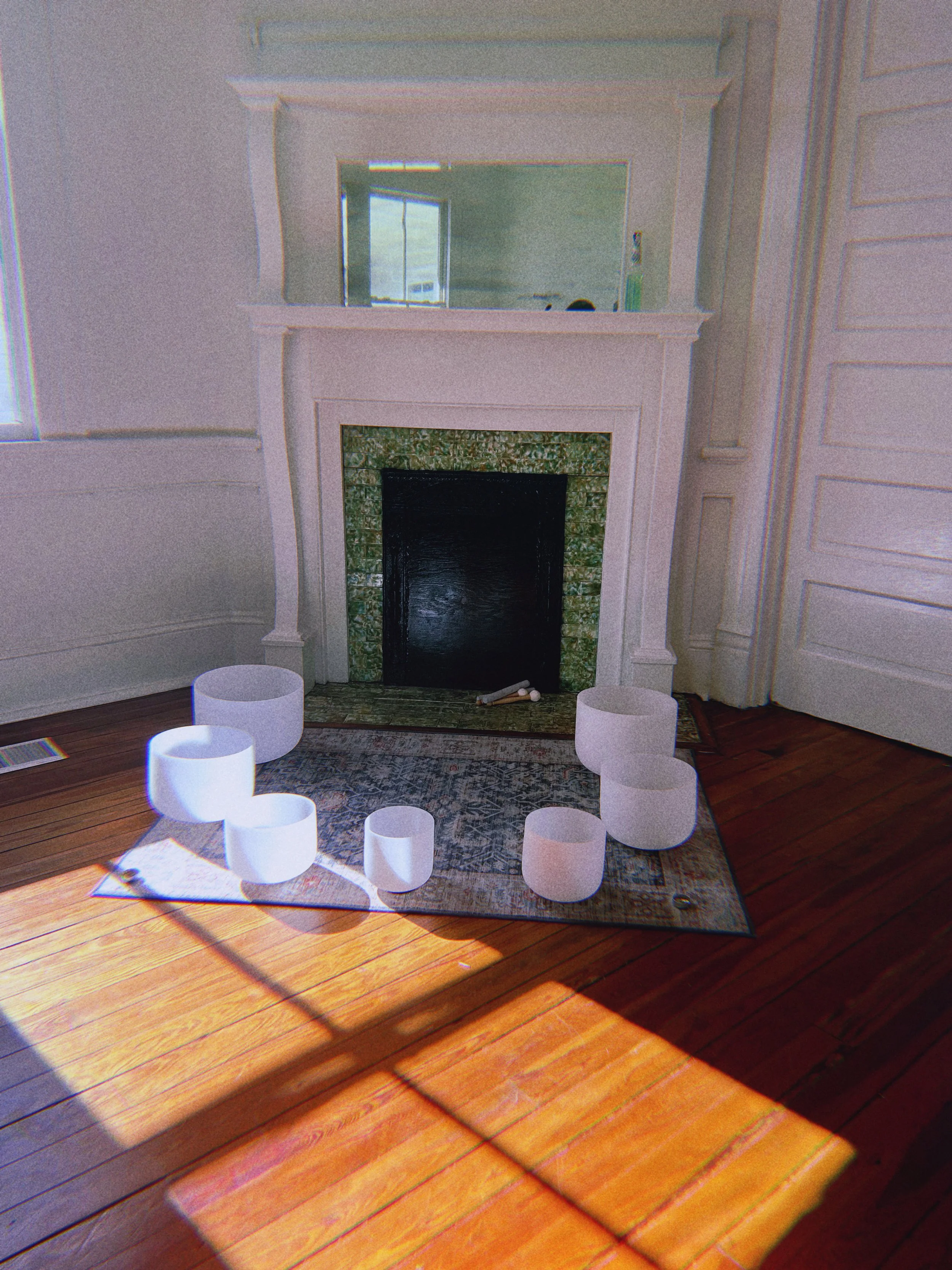 Living room with a decorative white fireplace, large mirror above it, and a colorful vase-shaped decor on the floor, illuminated by sunlight through a nearby window.