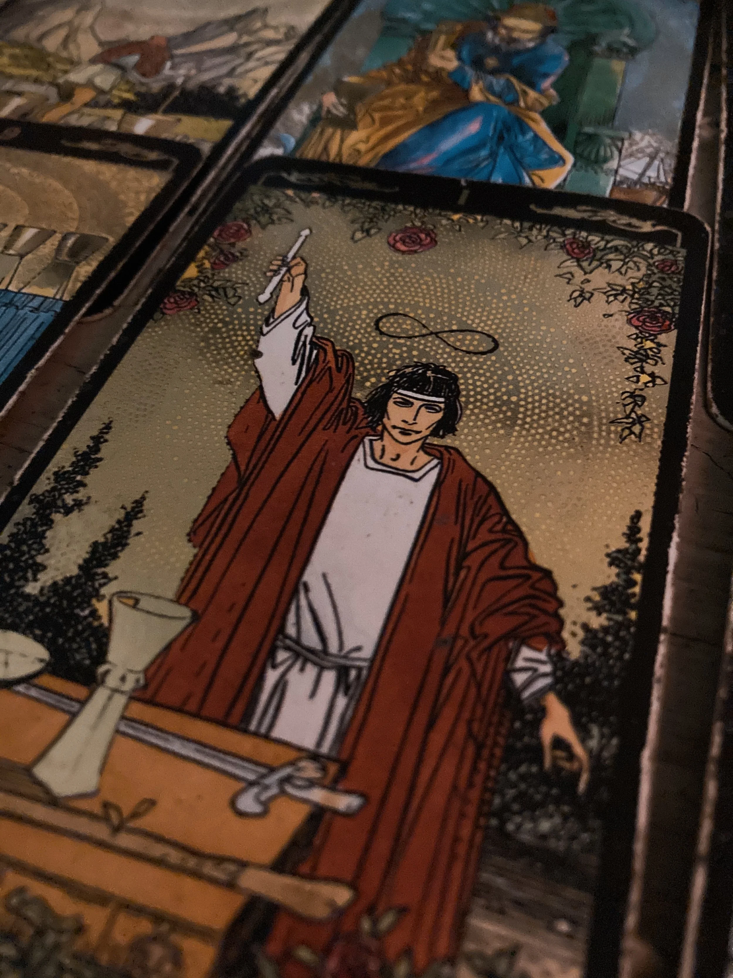 A tarot card depicting a woman in a red cloak holding a staff, with a symbol of infinity above her head, and various tools on a table in front of her.