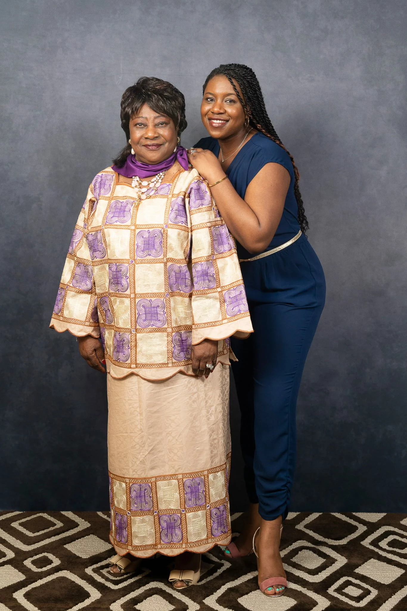 Tahirah, in a blue dress, stands lovingly next to her mother as they both smile warmly at the camera.