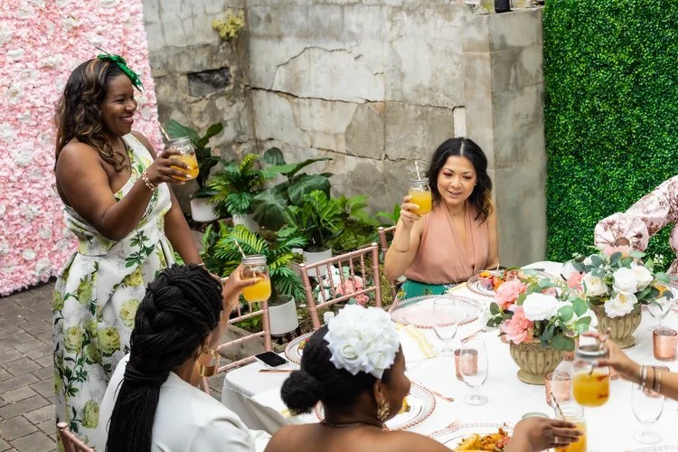 Non-Profit Event Planner Tahirah dressed in a green floral print gown while toasting at an upscale event.
