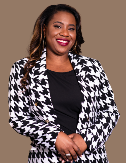 Tahirah wears a black and white houndstooth blazer and stands smiling brightly at the camera.