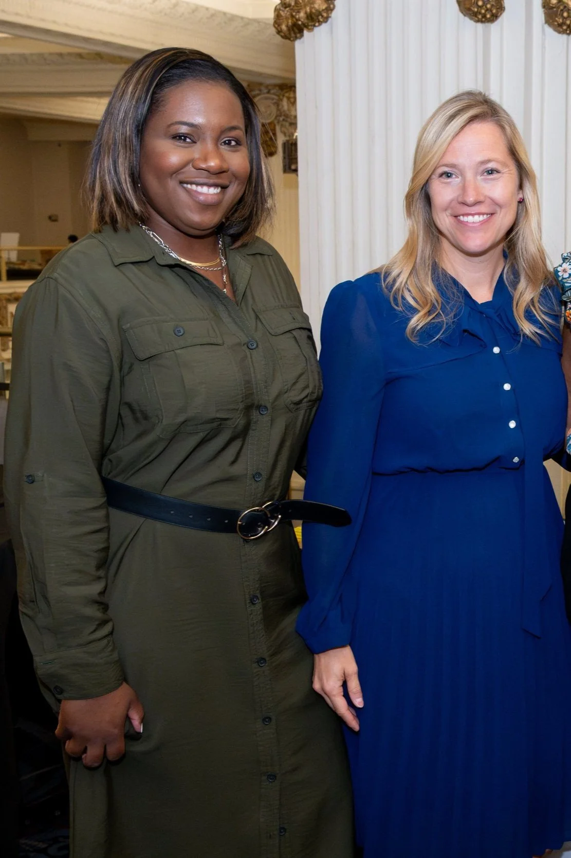 Corporate event planner Tahirah wears a green button down dress and stands with one of her non-profit corporate clients as they both smile warmly at the camera.