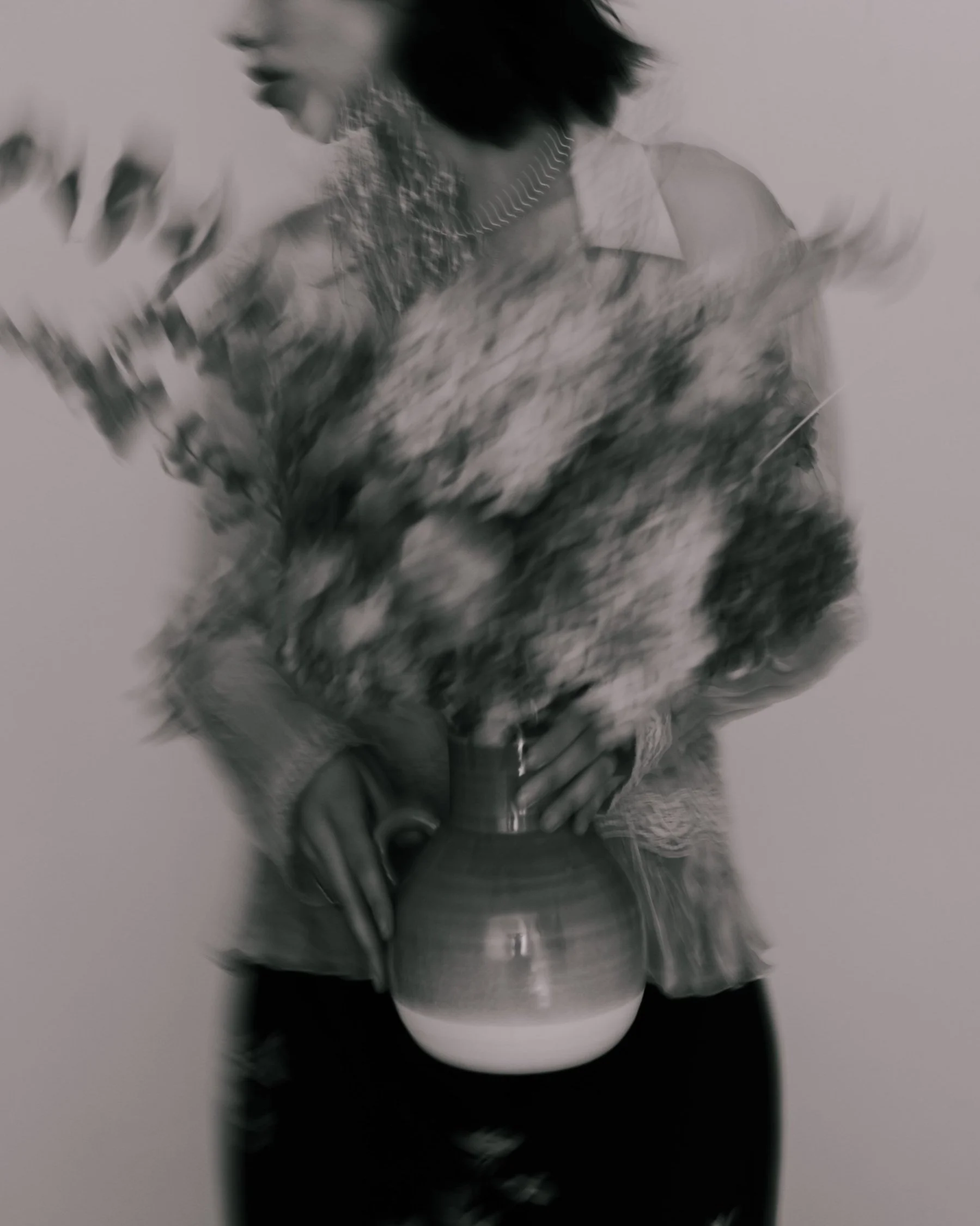 A woman holding a floral bouquet in a vase, wearing a light-colored shirt with embroidery, with blurred motion in the photo.