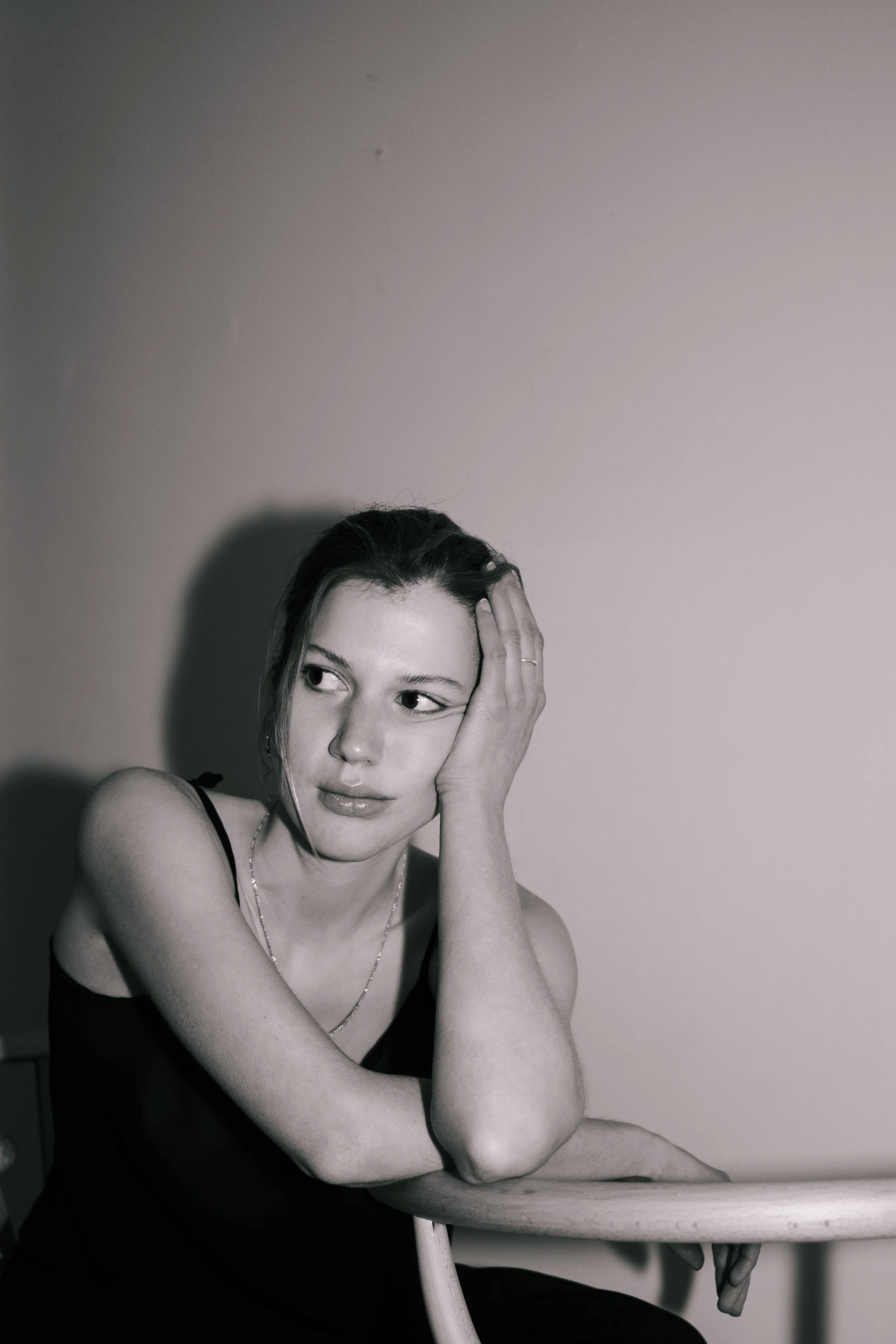 A woman sitting at a table with her head resting on her hand, looking thoughtful in black and white.